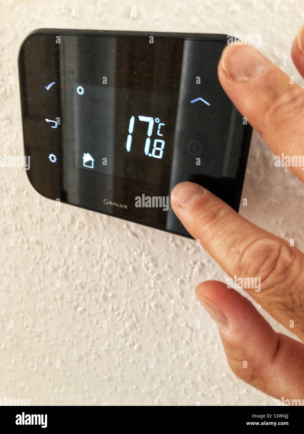 Proprietario di abitazione regolare il termostato centrale di stanza di riscaldamento del gas più basso per risparmiare sui costi di combustibile di spiraling ed il costo di crisi vivente - Immagine stock catturata con smartphone