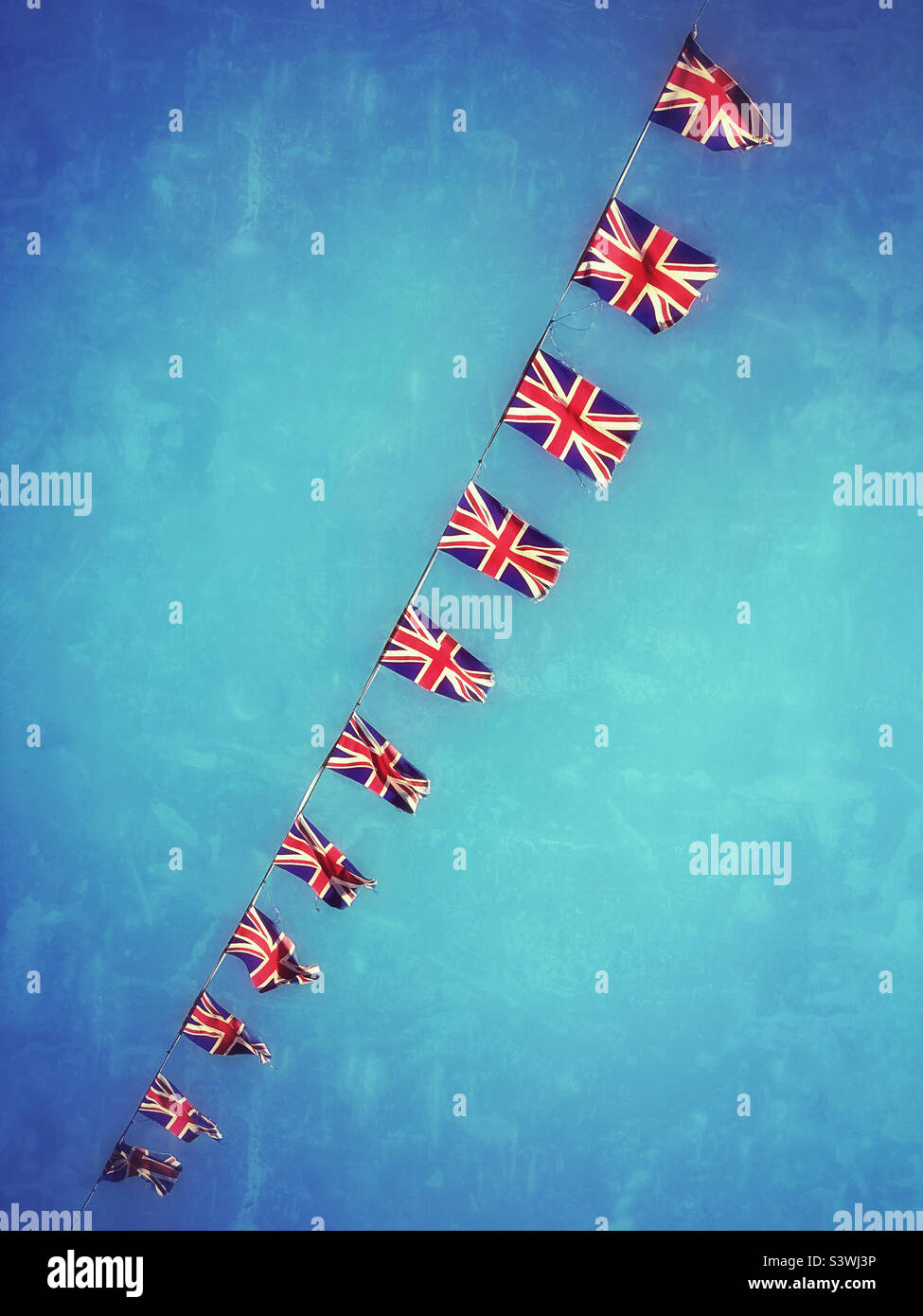 Un'immagine grunge e retrò di una linea di bandiere Union Jack. Bunting, balbettando nel vento di un'estate britannica, celebrando il Platinum Jubilee della Regina. Foto ©️ COLIN HOSKINS. Foto Stock