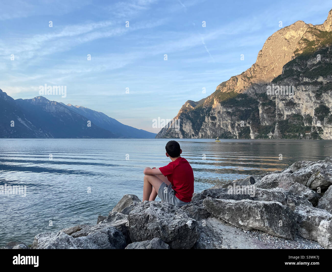 Un momento memore che riflette sulla vita guardando su un tranquillo lago di Garda verso le montagne. Foto Stock