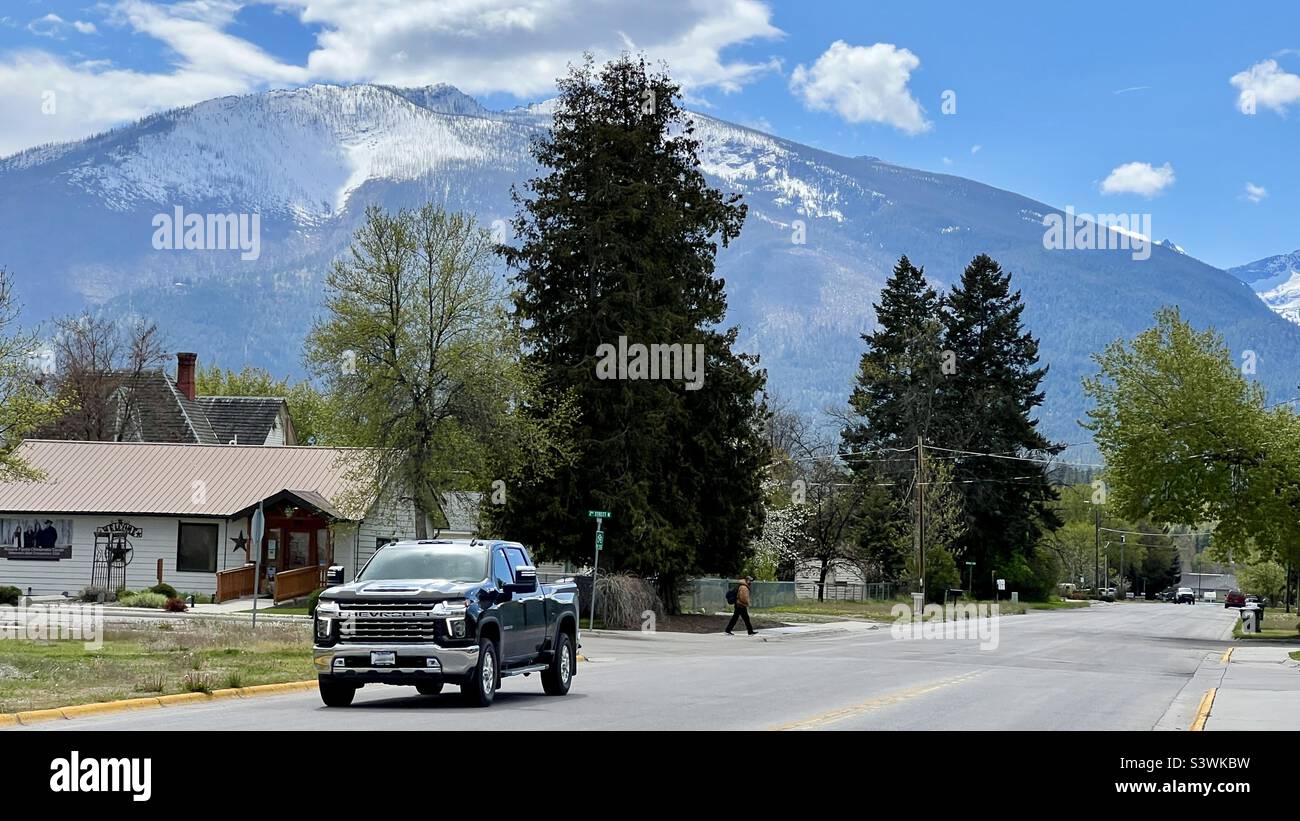 HAMILTON, MT, MAGGIO 2022: Camion pick-up nero guida su strada rurale, con alberi dietro, e piccole nuvole bianche sulle montagne sullo sfondo Foto Stock