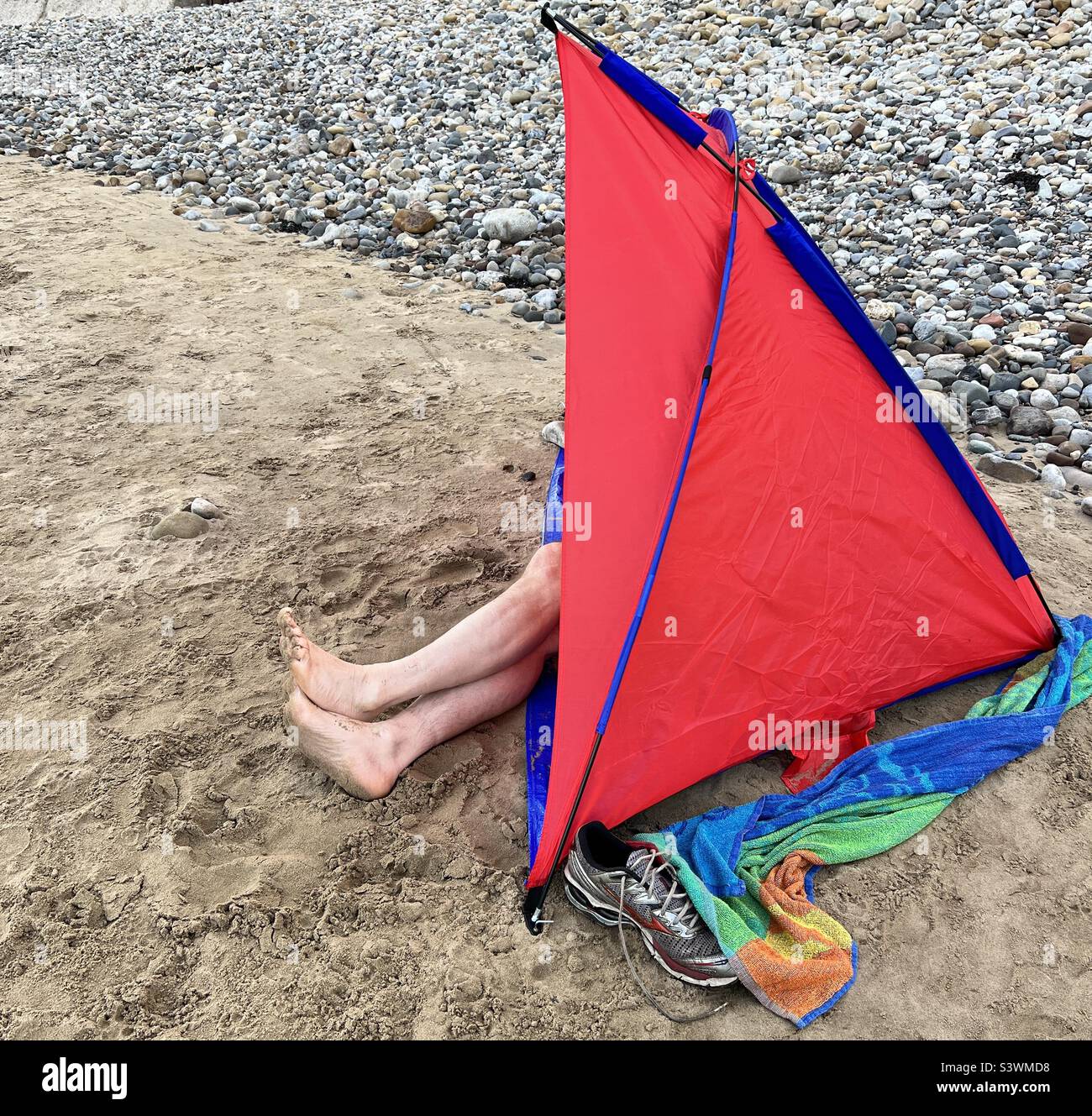 Uomo in una tenda da spiaggia rossa con le gambe che sporgono - Immagine stock catturata con smartphone