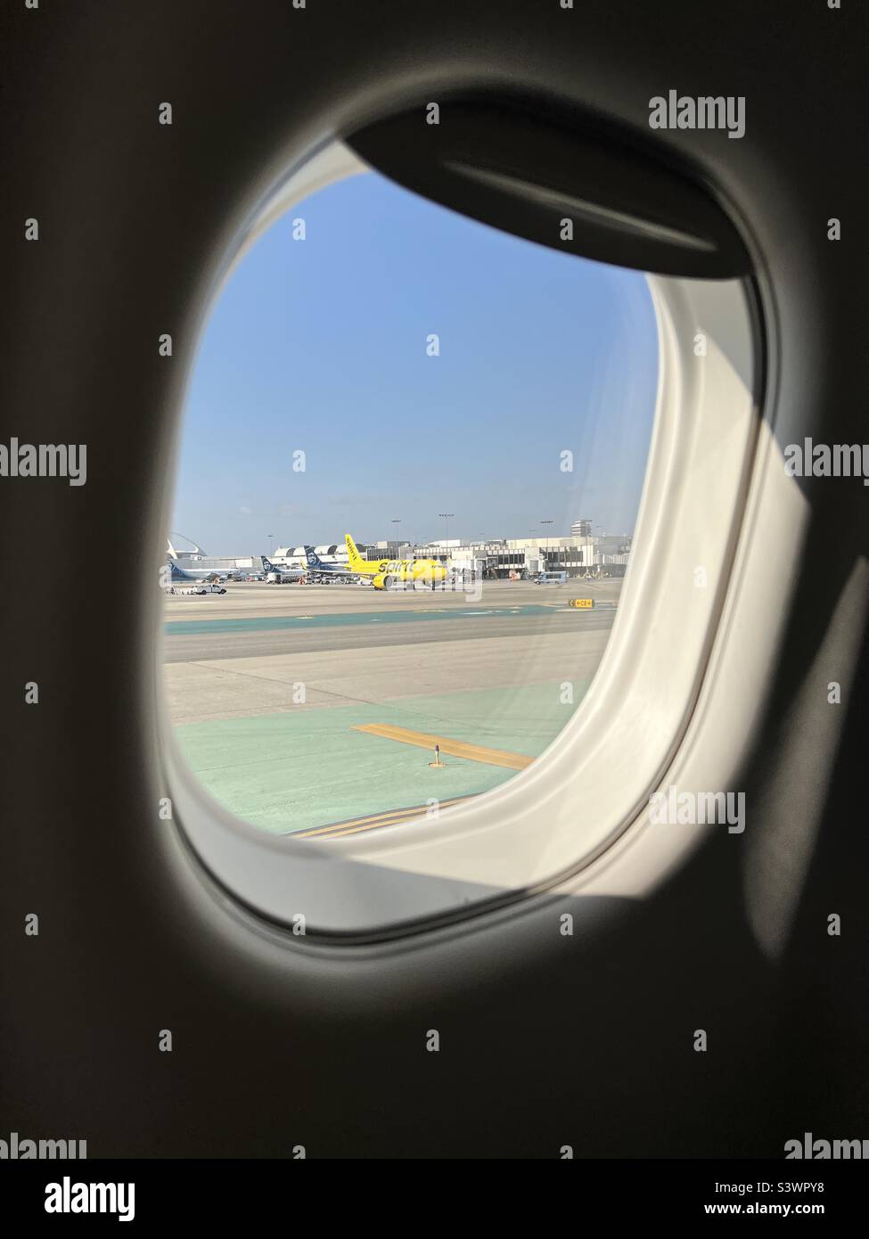 LOS ANGELES, CA, 2022 GIUGNO: Il jet Spirit Airlines giallo brillante all'aeroporto internazionale di Los Angeles, visto attraverso la finestra di un altro aeromobile passeggeri Foto Stock