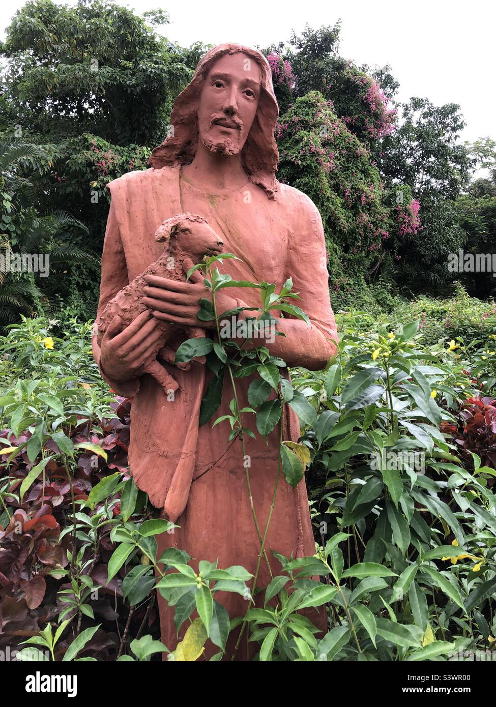 Statua in terracotta a grandezza naturale di Gesù Cristo che tiene un agnello in un cimitero cattolico a Saligao, Goa, India. Foto Stock