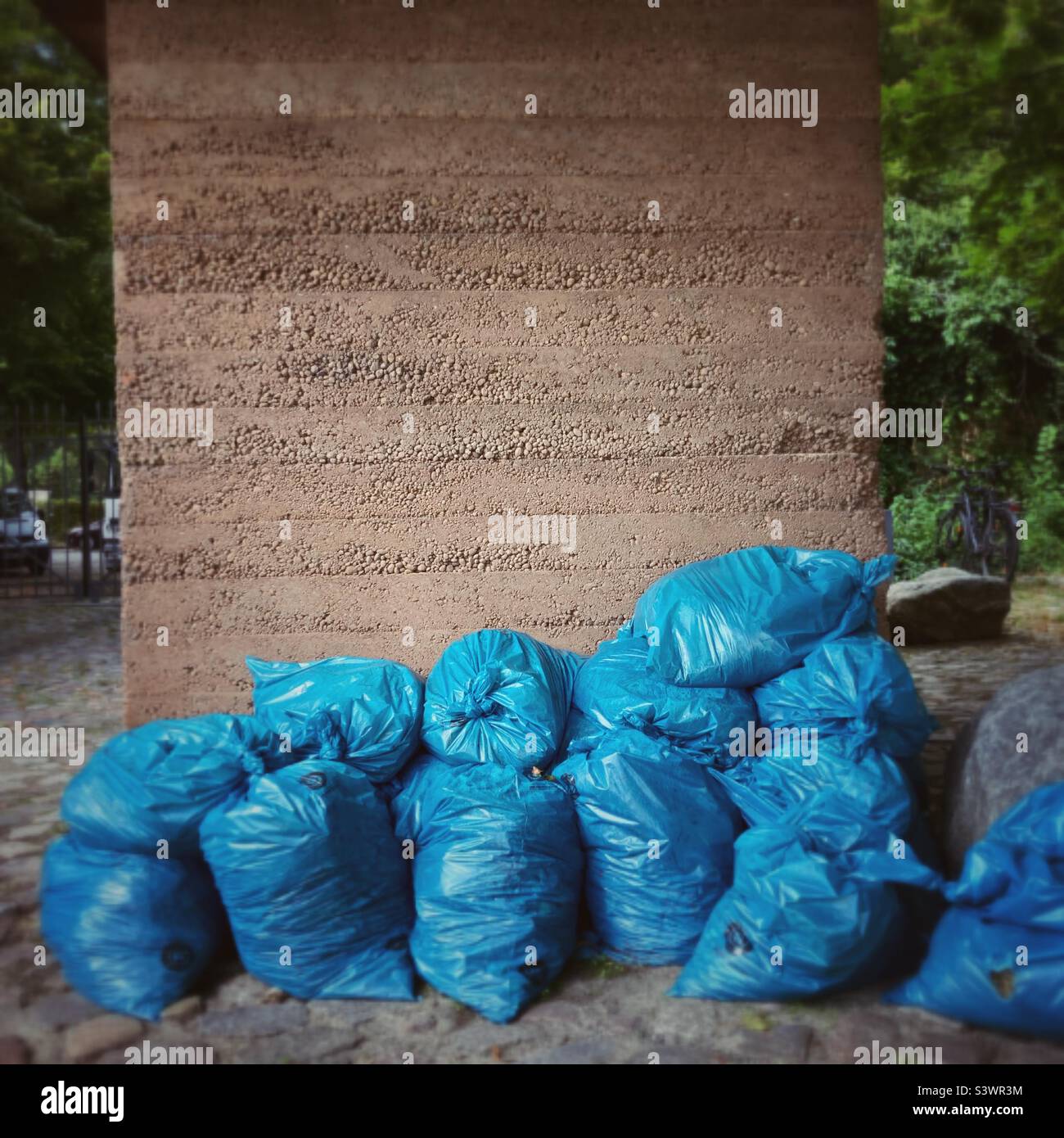 Un mucchio di sacchi di spazzatura blu davanti ad un muro di cemento Foto Stock