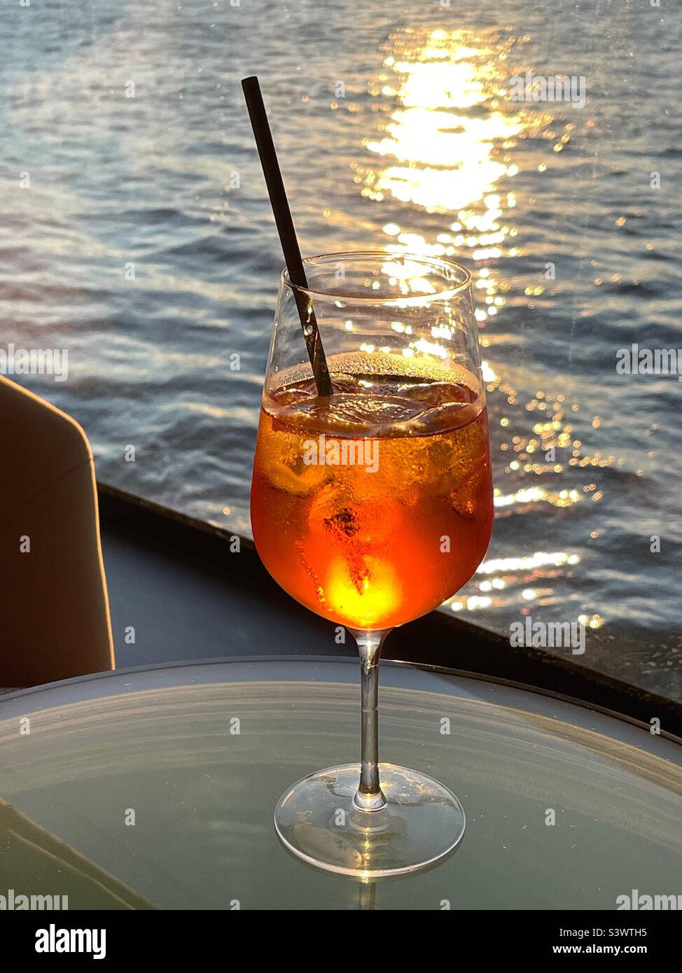 Bicchiere di Aperol Spritz sullo sfondo del sole tramontato sull'acqua Foto Stock