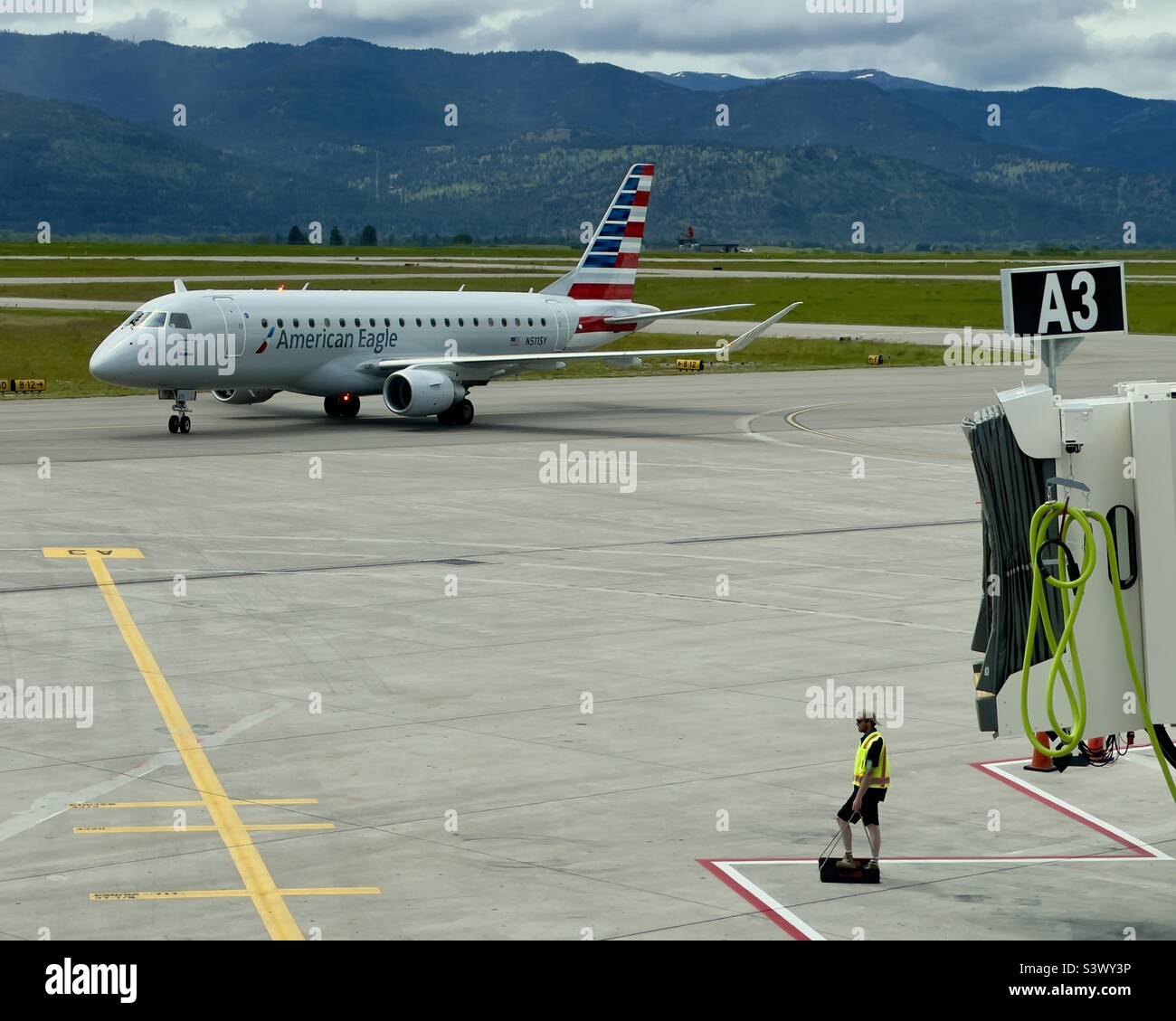 MISSOULA MONTANA AIRPORT, MT, GIUGNO 2022: American Airlines Embraer E175 jet Aircraft si avvicina terminal, squadra di terra in primo piano, montagne sullo sfondo Foto Stock