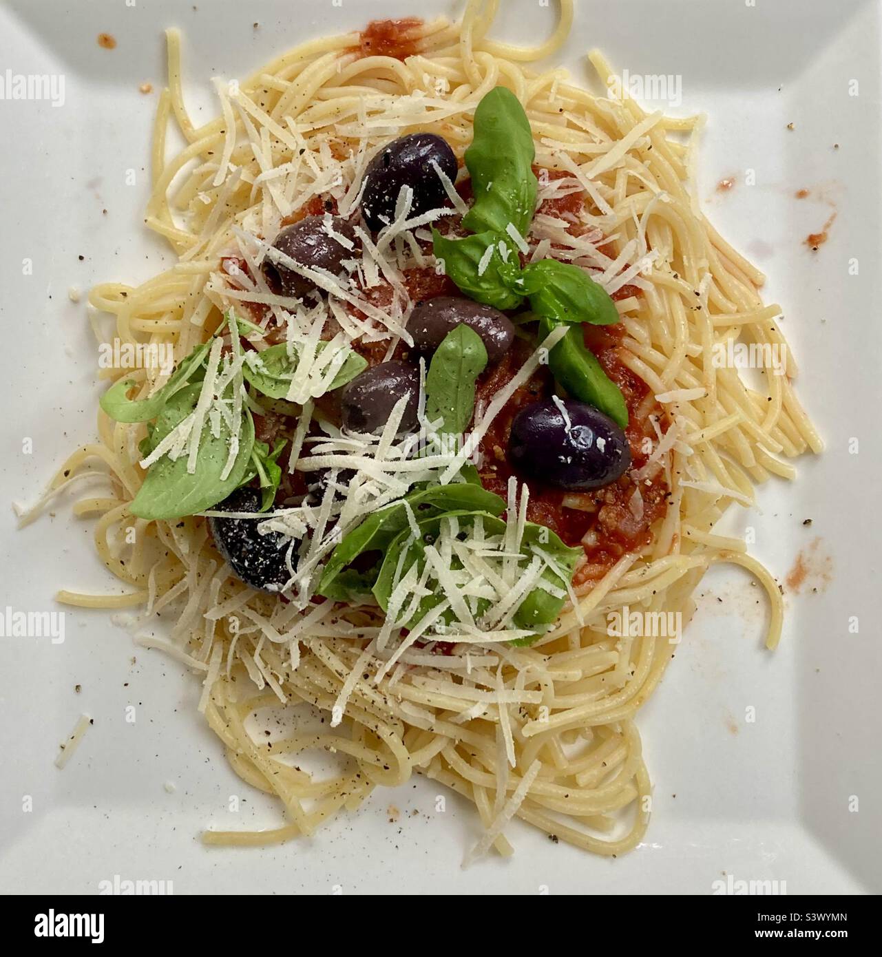 Spaghetti fatti in casa con pasta senza glutine, conditi con olive Kalamata, basilico fresco raccolto nel giardino, parmigiano reggiano e pepe fresco crackizzato. Foto Stock