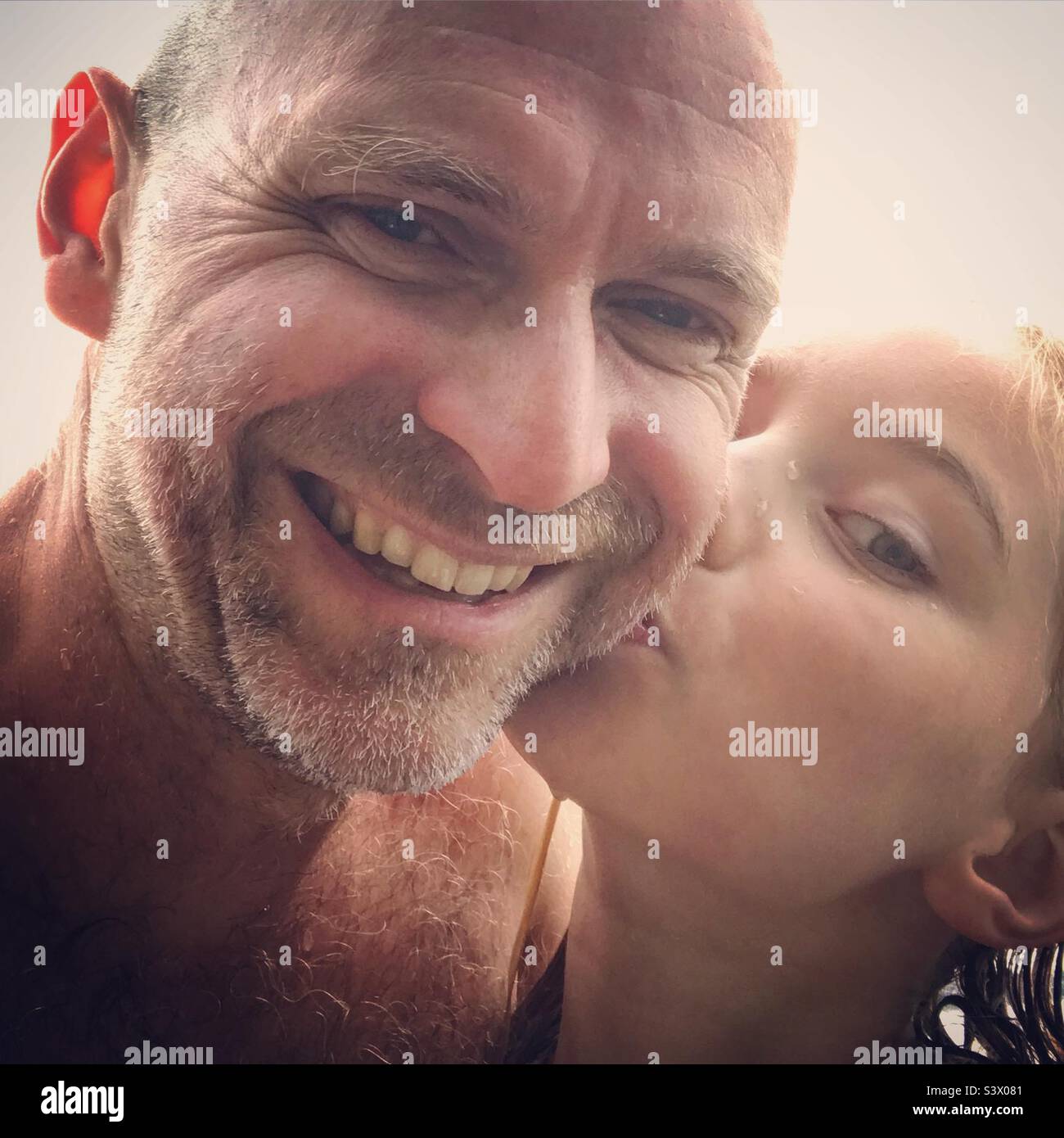 Figlia baciando suo padre sulla guancia durante una vacanza sulla spiaggia condividendo la famiglia felice tempo insieme sorridendo Foto Stock