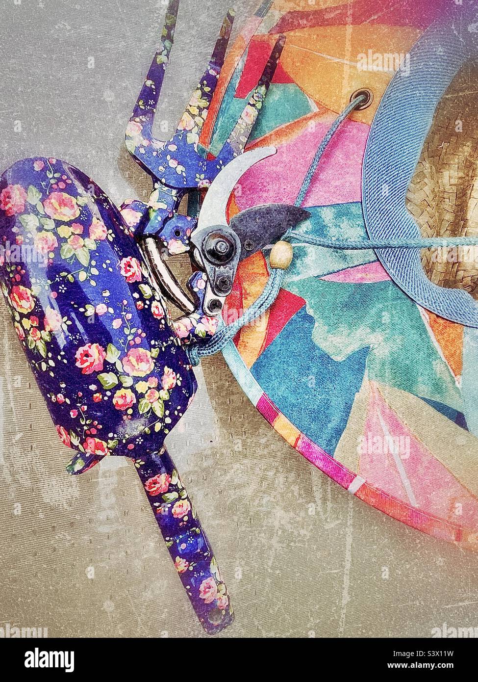 Attrezzi di una donna giardiniera per lavorare nel suo cortile/giardino - un cappello di paglia colorato, e cesoie per potare fiori, vanga e artiglio. Effetto grunge aggiunto digitalmente a questa vita morta all'aperto. Foto Stock