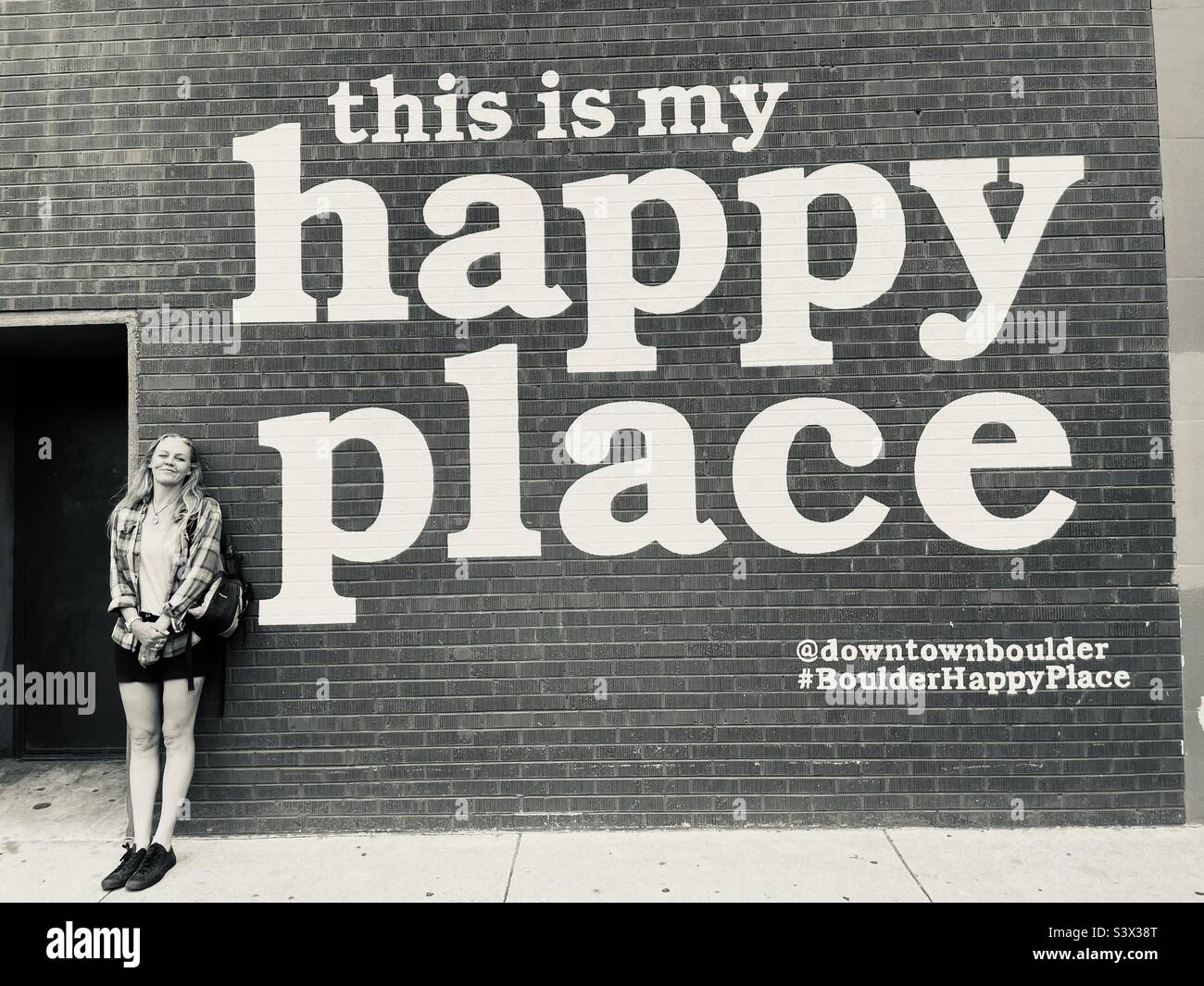Una donna si trova accanto a un grande cartello su un muro a Denver, Colorado - Immagine stock catturata con smartphone