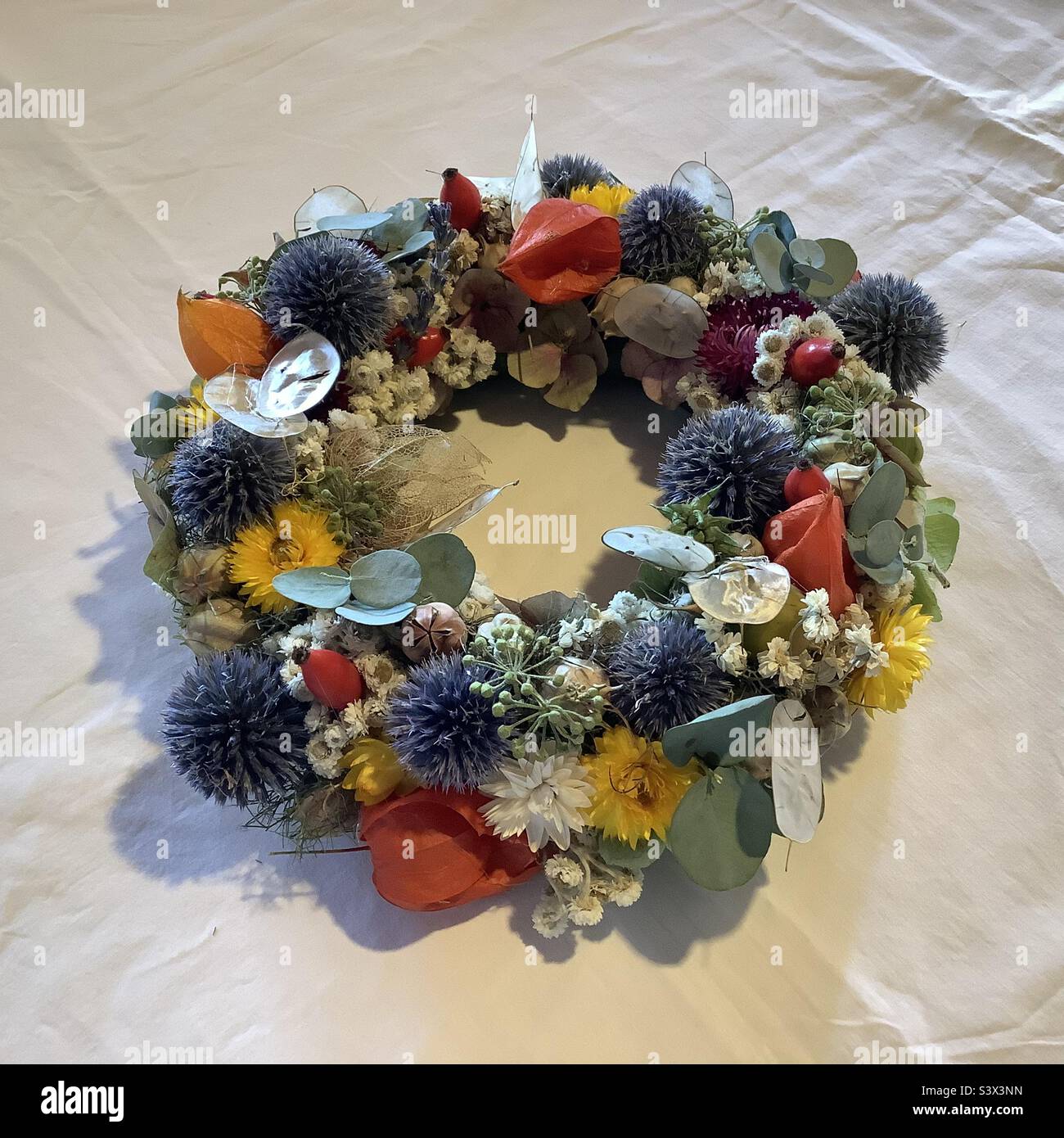 Corona floreale intrecciata a mano creativa con fiori da giardino su tovaglia bianca Foto Stock