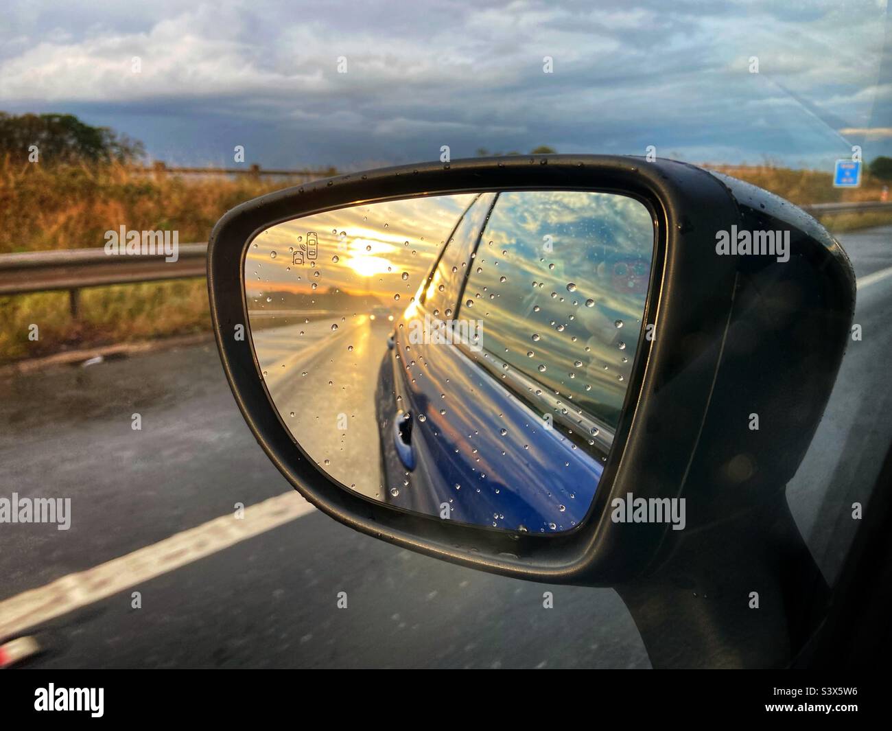 Vista del tramonto sullo specchio d'ala se l'auto blu è in autostrada Foto Stock
