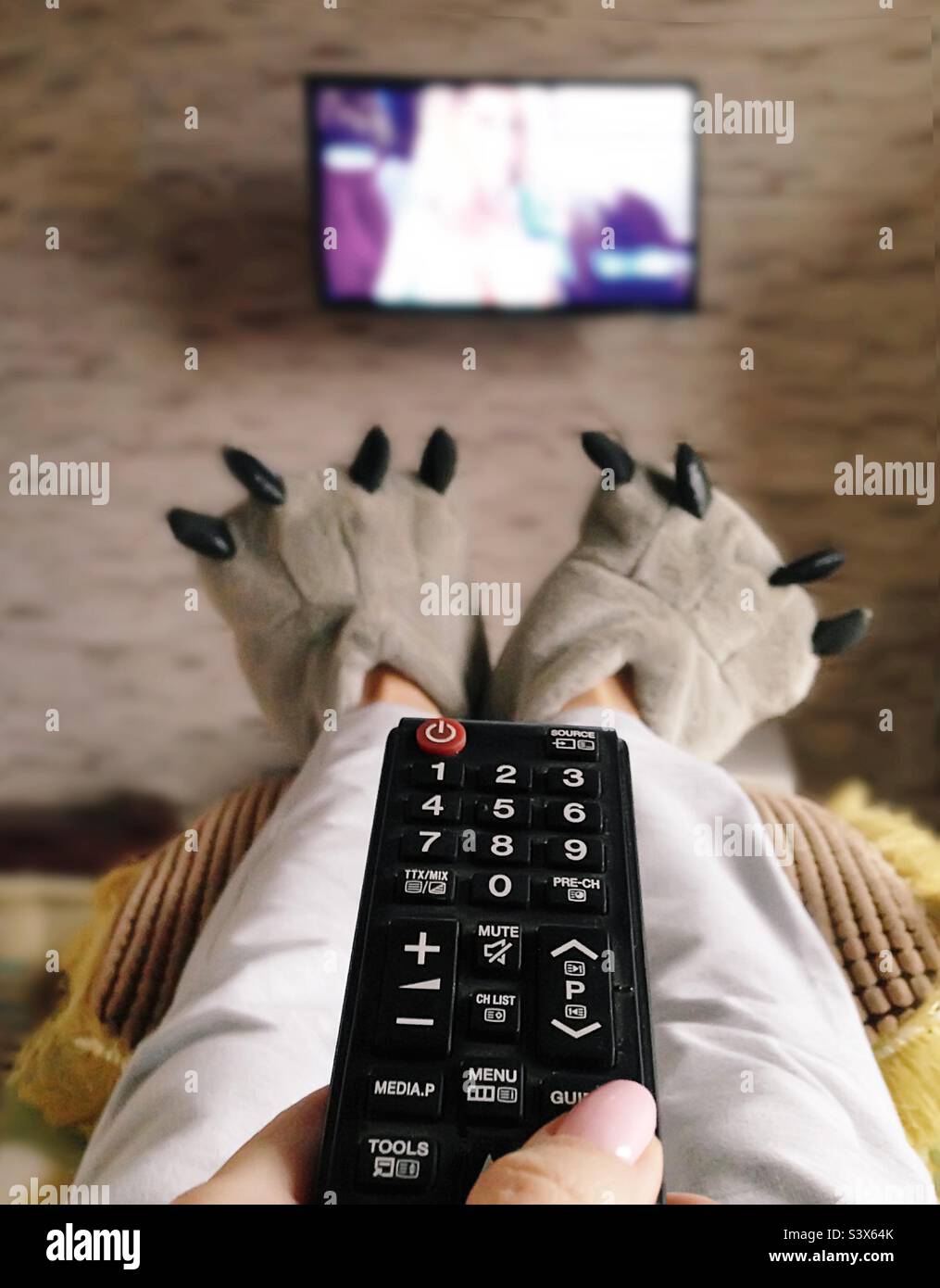 Guardare la televisione in divertenti pantofole a casa - Immagine stock catturata con smartphone