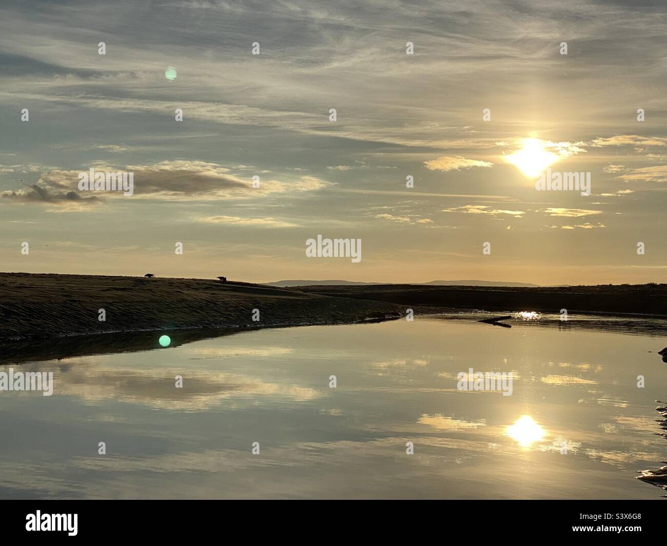 Sole basso e nubi eflections in un fiume lento Foto Stock