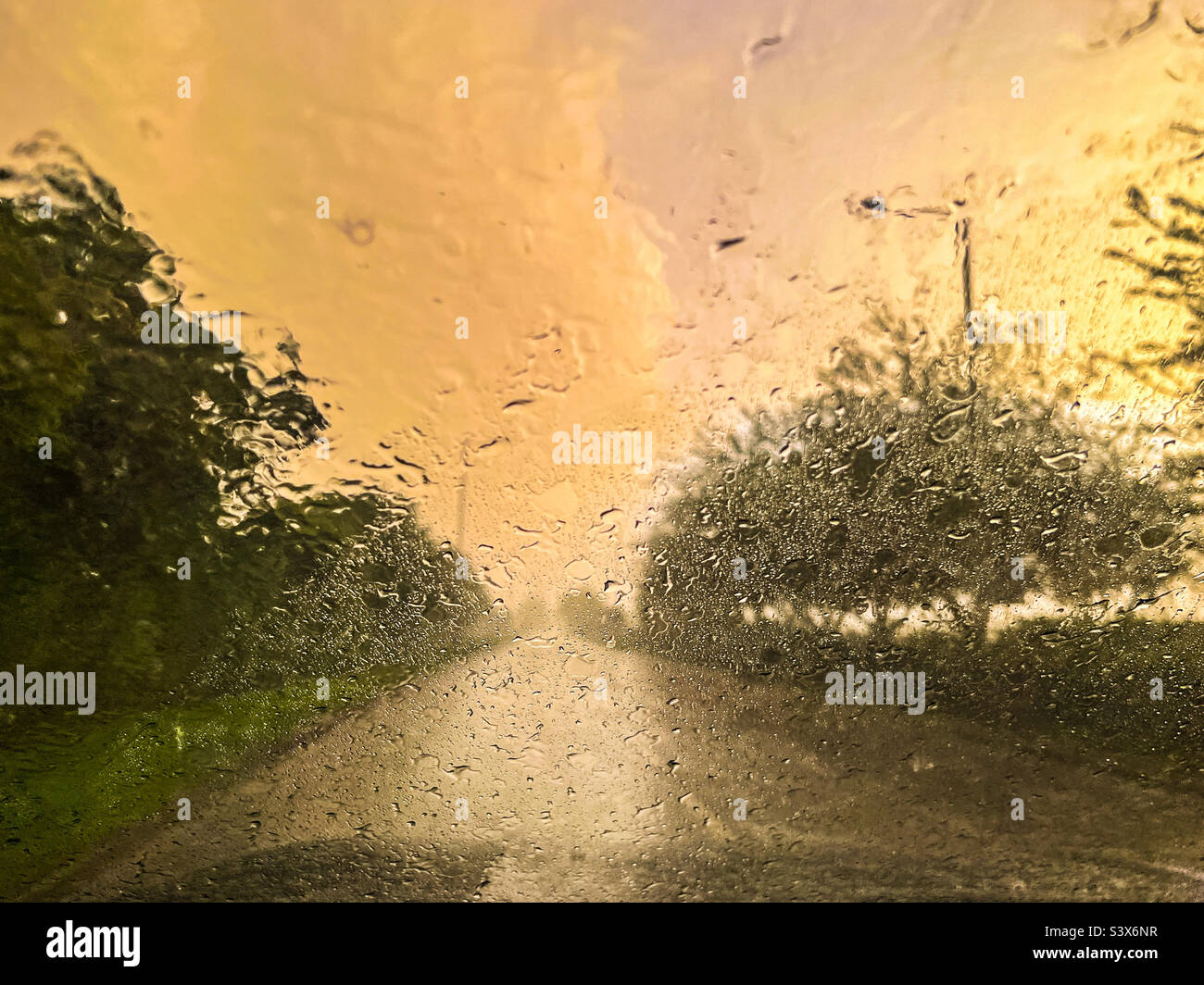 Pioggia sul finestrino dell'auto durante il tramonto su una strada di contea Foto Stock