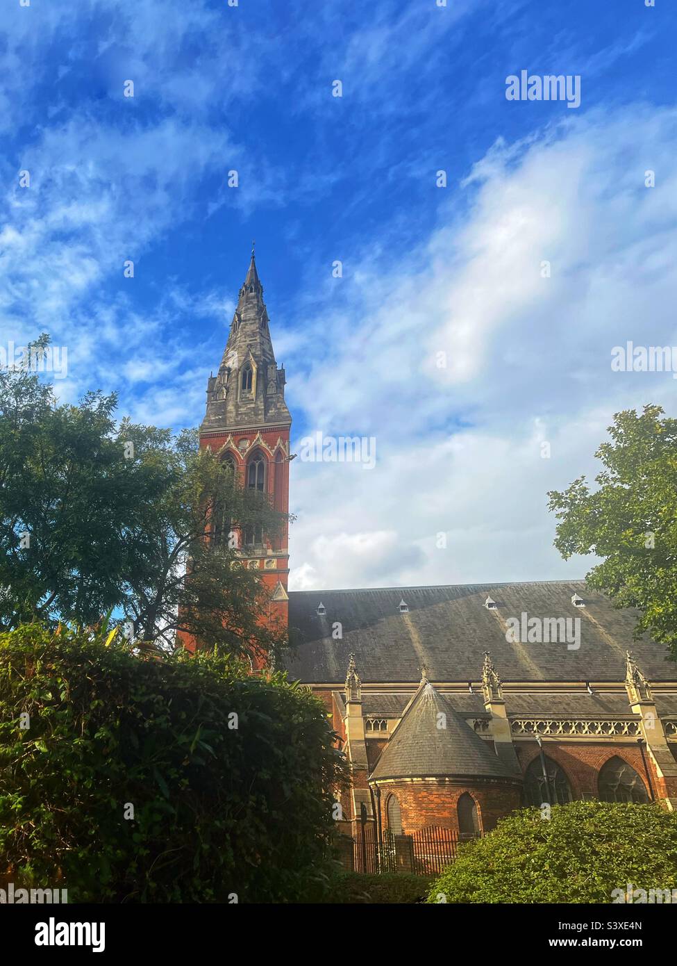 Vista di St John the Divine, Kennington, South East London, edificio classificato di primo livello, visto dai Giardini Dan Leno - Dan Leno vissuto nelle vicinanze - la guglia della chiesa è imponente e ha un orologio. Foto Stock