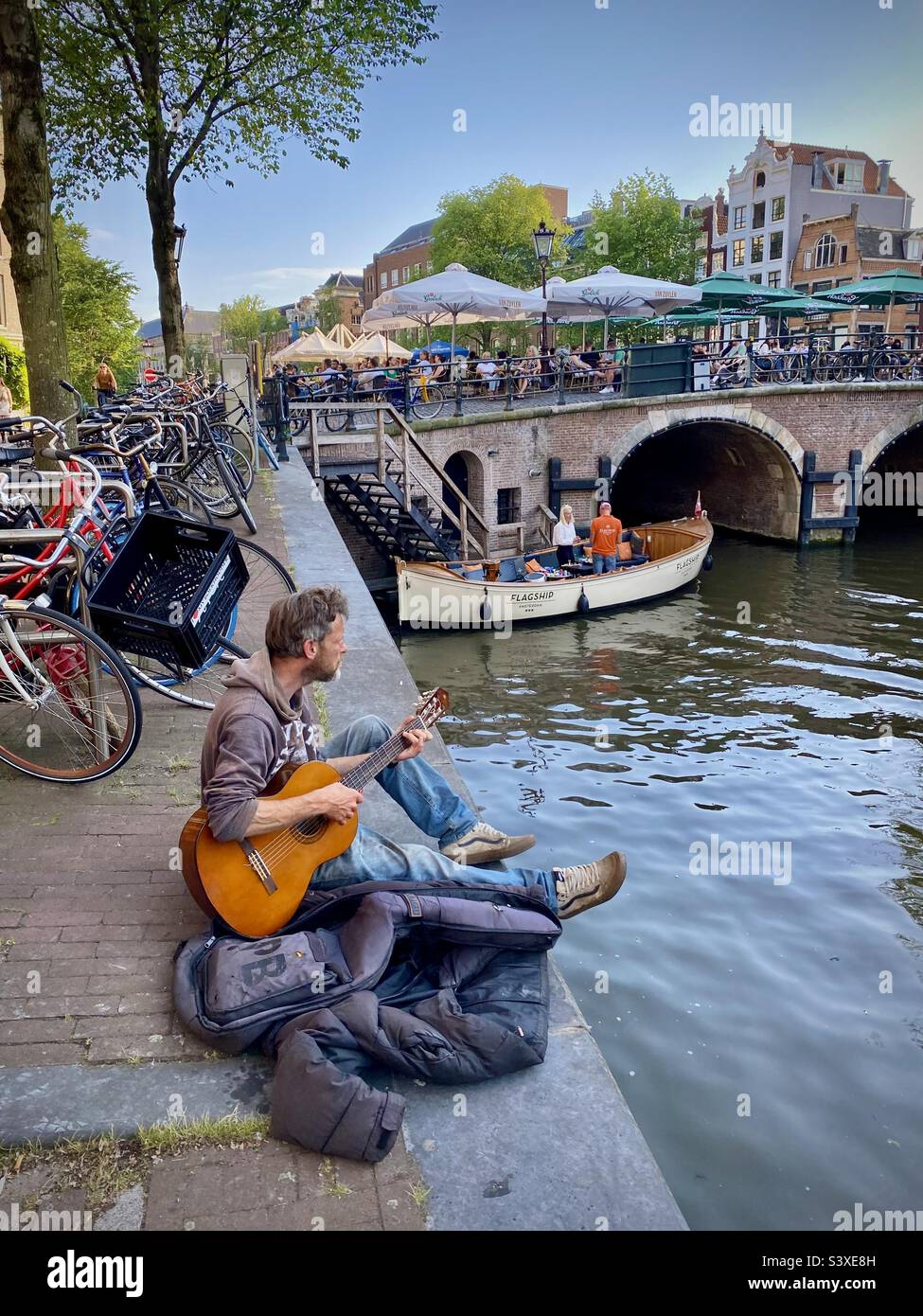 Un busker suona la sua chitarra seduto su un canale in una bella serata estiva durante l'ora d'oro nel cuore di Amsterdam Foto Stock