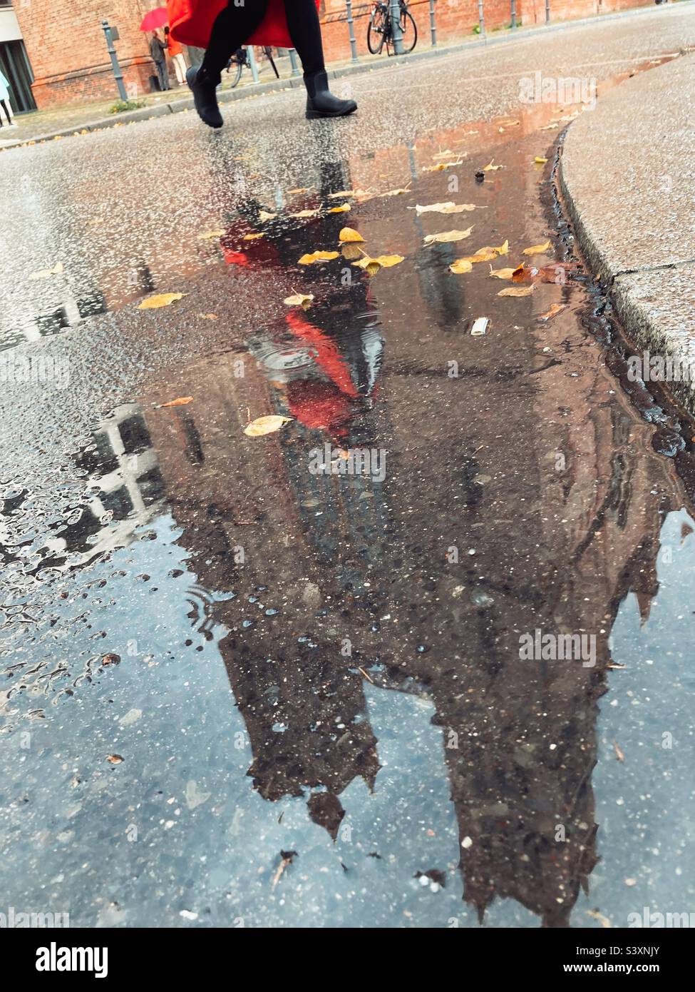 La facciata anteriore e i campanili della Chiesa di Friedrichswerder si riflettono in una pozza con una donna in stucco rosso Passeggiate in autunno, Berlino, Germania - Immagine stock catturata con smartphone