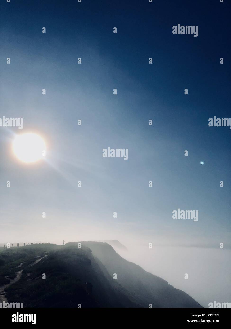 Un uomo in lontananza si trovava sulla cima di una scogliera al tramonto Foto Stock