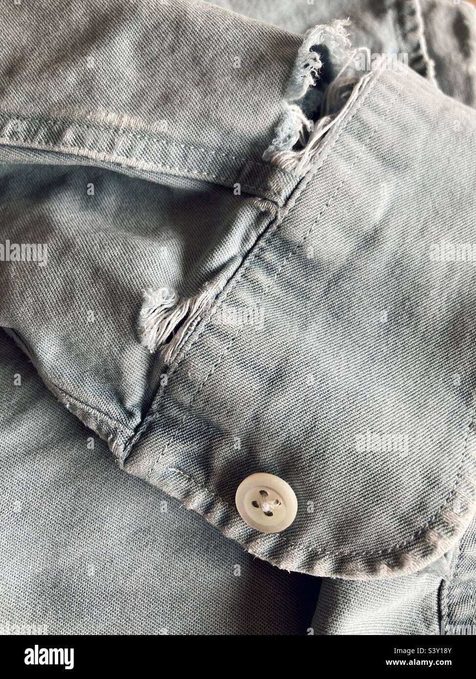 Il gambaletto sfilacciato di una camicia in denim Foto Stock