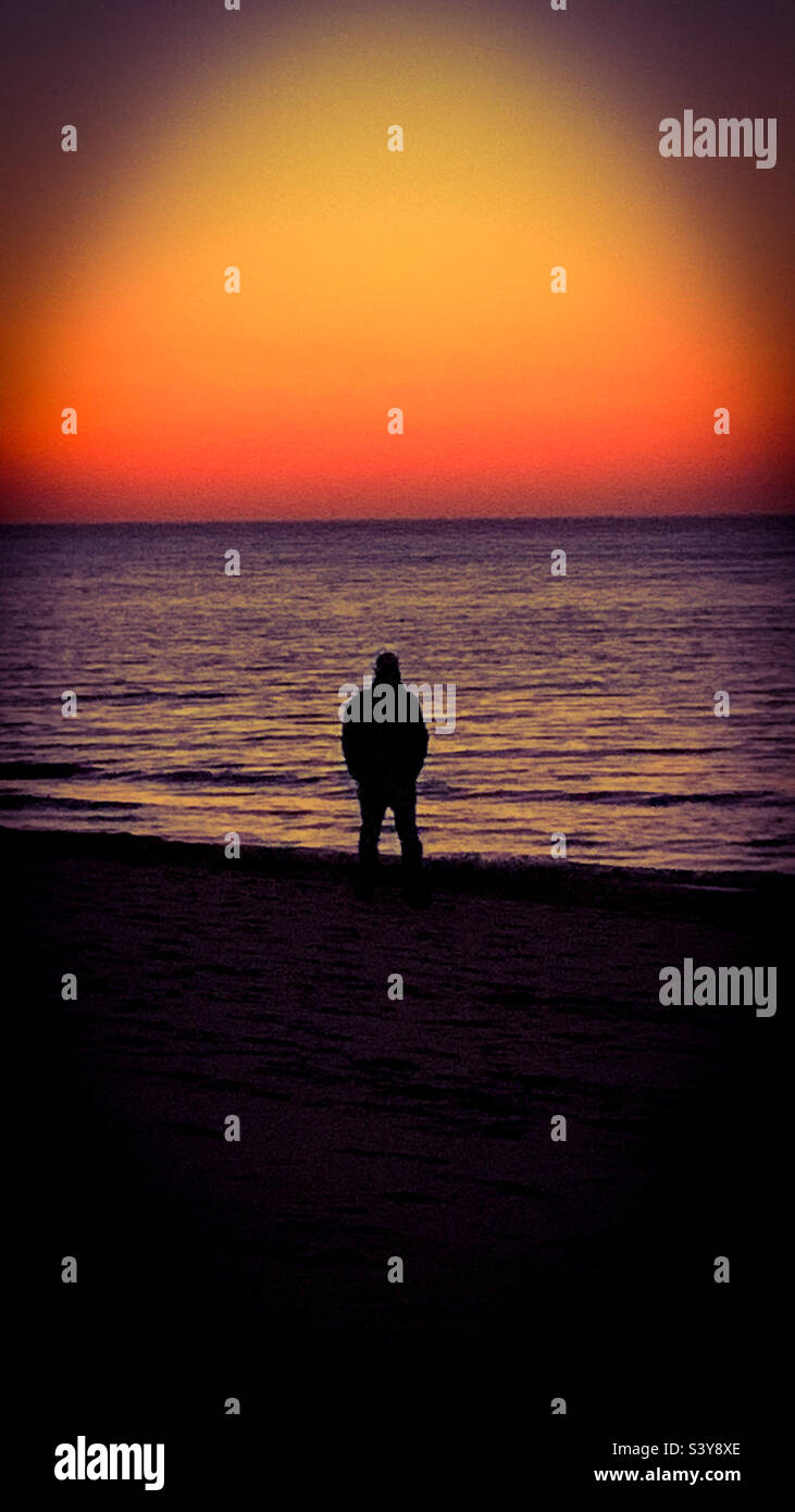 Uomo a camminare sulla spiaggia al tramonto Foto Stock