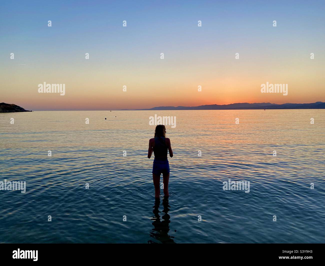 Ragazza in silhouette che paddling a Lardos Bay al tramonto. Pefkos sull'isola di Rodi, Grecia Foto Stock