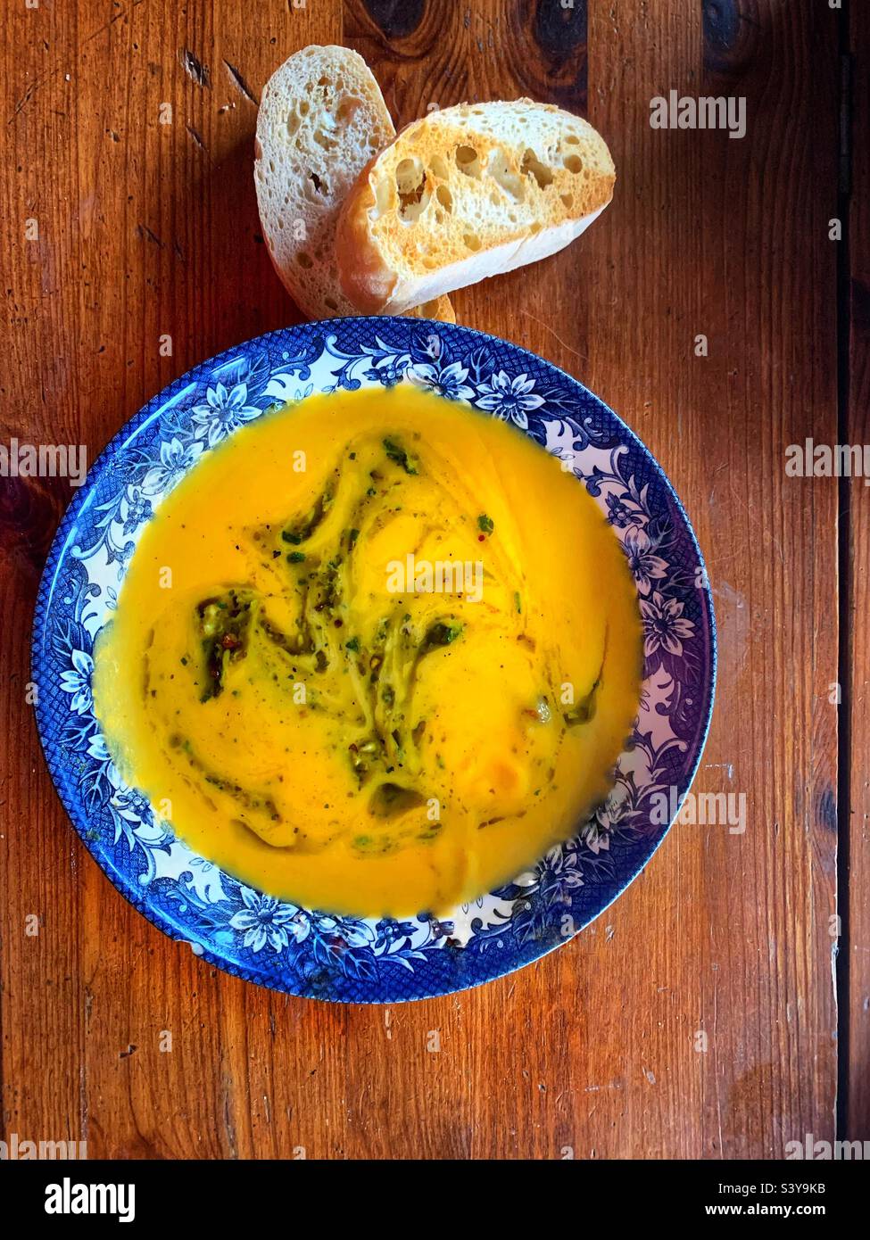 Zuppa di zucca fatta in casa con noci tritate, olio d'oliva, pesto al basilico, coriandolo fresco e 2 due fette di ciabatta tostata su un tavolo di legno Foto Stock