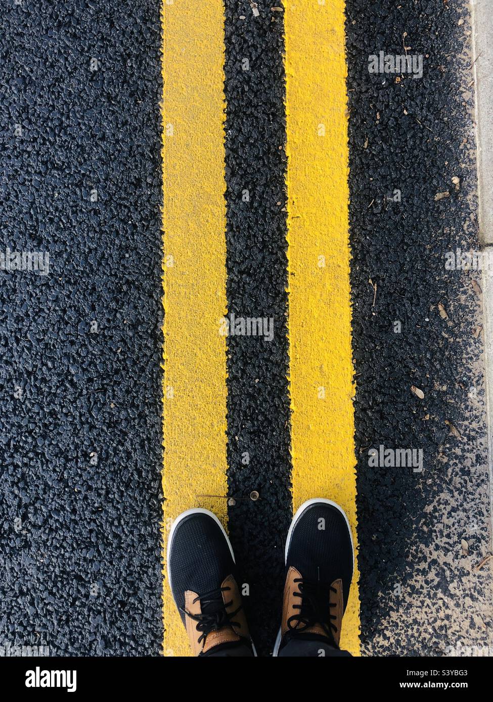 Persona in piedi sulle linee stradali gialle Foto Stock