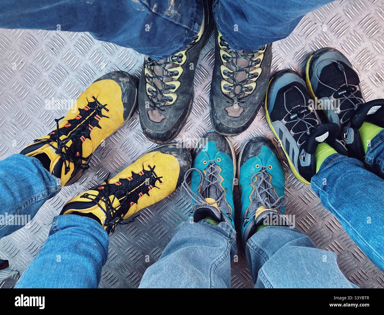 Quattro paia di gambe e piedi in scarponi da trekking POV sul pavimento metallico di un ascensore: Una famiglia sulla via del ritorno da un'escursione - Immagine stock catturata con smartphone