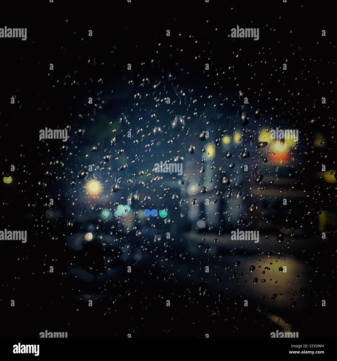 Una fotografia di un edificio con luci colorate accese di notte, attraverso gocce di pioggia su una finestra. Profondità di campo bassa. Fotografia notturna autunno scuro - Immagine stock catturata con smartphone