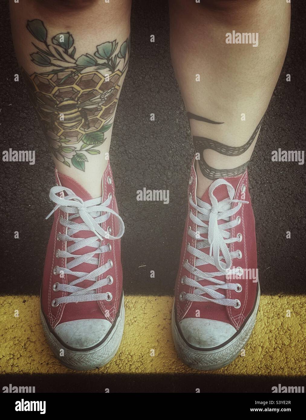 Guardando in basso le gambe tatuate di una giovane donna e le sneakers rosse alte Chuck Taylor. Foto Stock