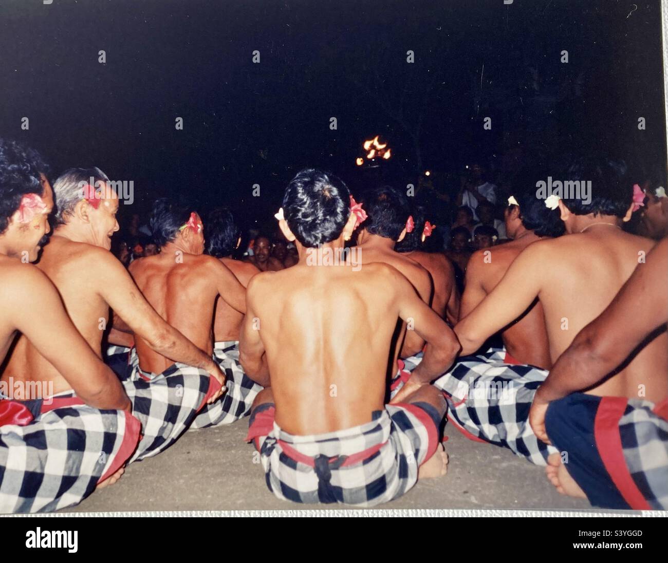 Gli uomini balinesi si siedono in fila mentre si esibiscono in danze e canzoni tradizionali. Foto Stock