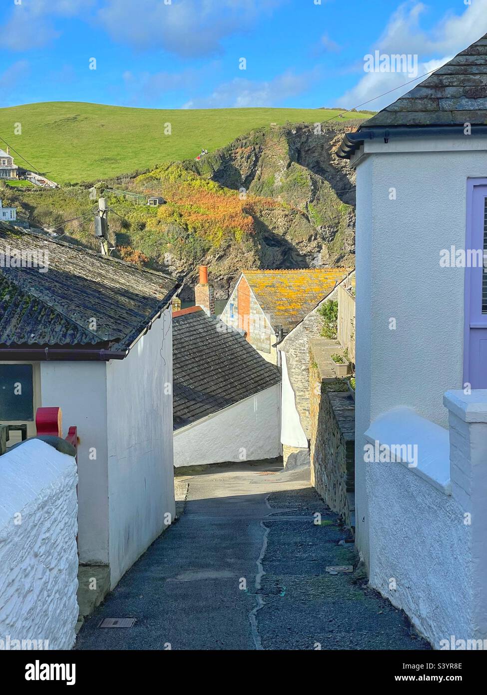 Strada stretta a Port Isaac, con scogliere sul mare oltre, Cornovaglia Nord. Foto Stock