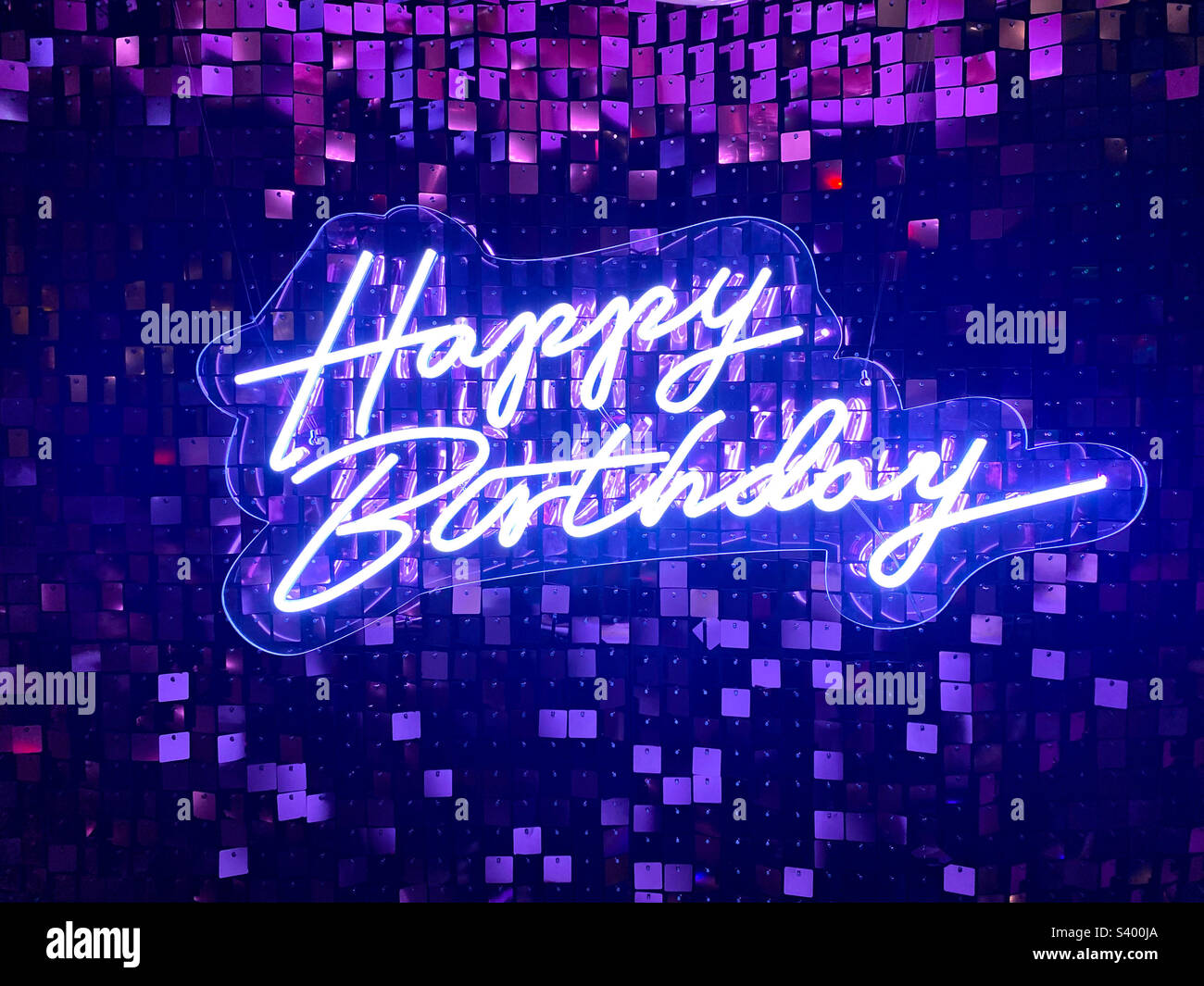 Insegna bianca illuminata Happy Birthday su uno sfondo viola brillante. Foto Stock