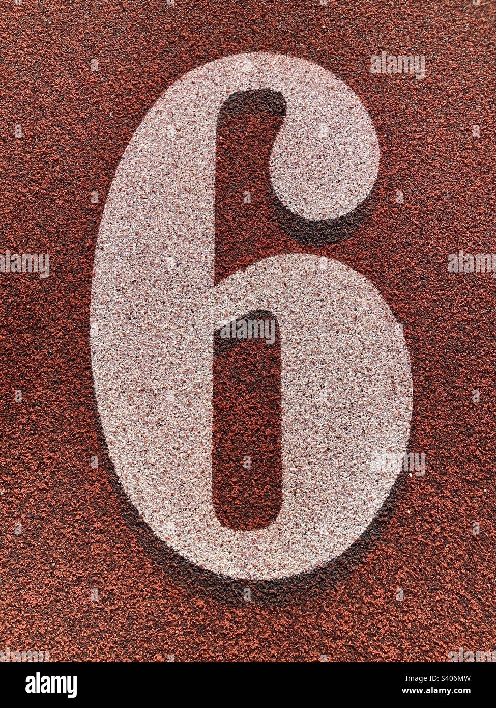 Il numero sei (6) sul tappeto erboso e sul campo. Scritta bianca con sfondo rosso a trama. Foto Stock