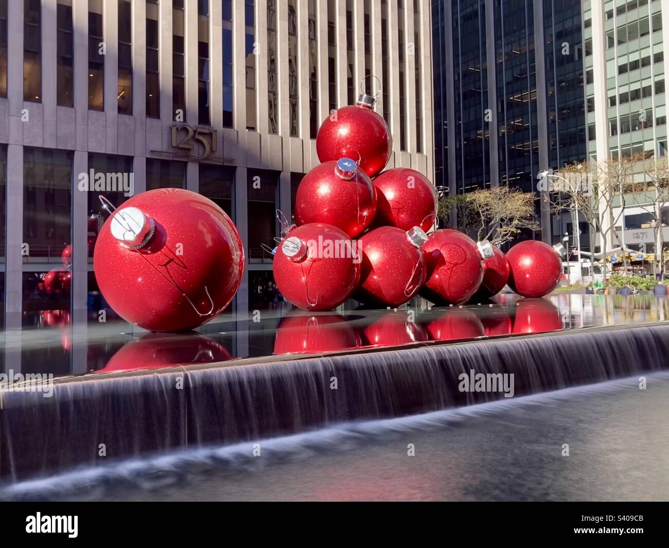 Grandi ornamenti rossi per le vacanze sulla 6th Ave., Avenue of the Americas, nel centro di Manhattan, New York, con una lunga esposizione sulla parte della cascata - Immagine stock catturata con smartphone