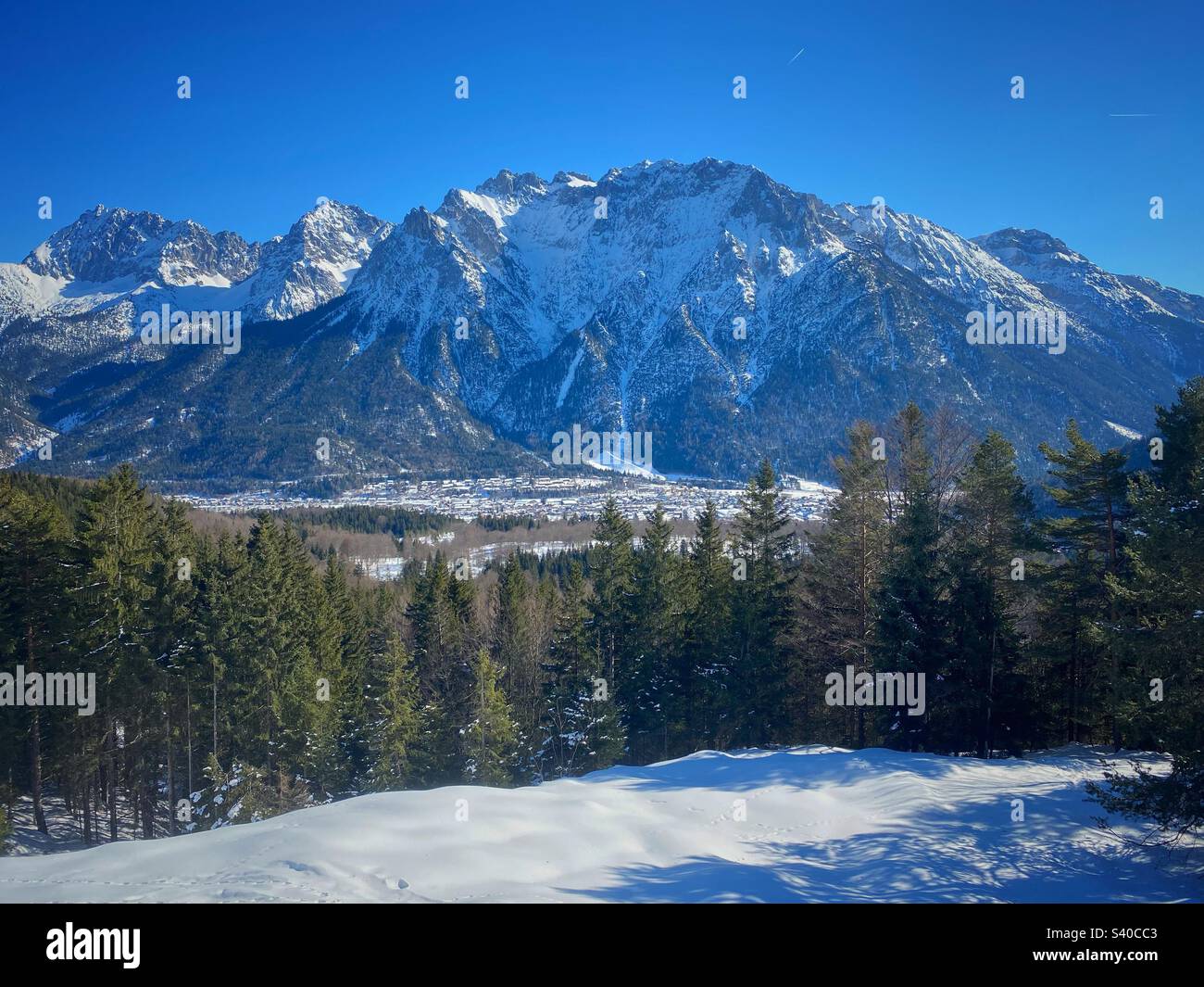 Vista innevata invernale su pini, vette alpine e parte della città di Mittenwald dalla cima del monte Kranzberg nella Germania meridionale. Foto Stock