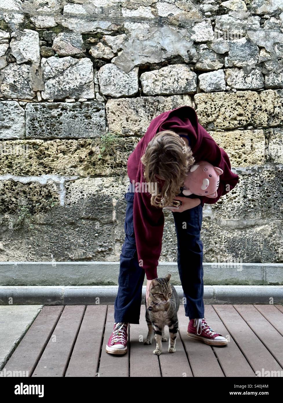 L'adolescente accarezza un gatto mentre tiene un gatto coccolato giocattolo Foto Stock