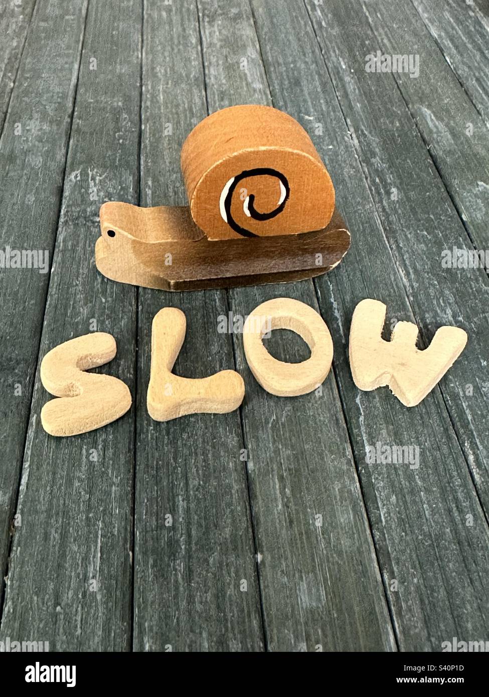 Testo lento, composizione concettuale con lettere di legno fatte a mano e una miniatura di lumaca di legno - Immagine stock catturata con smartphone