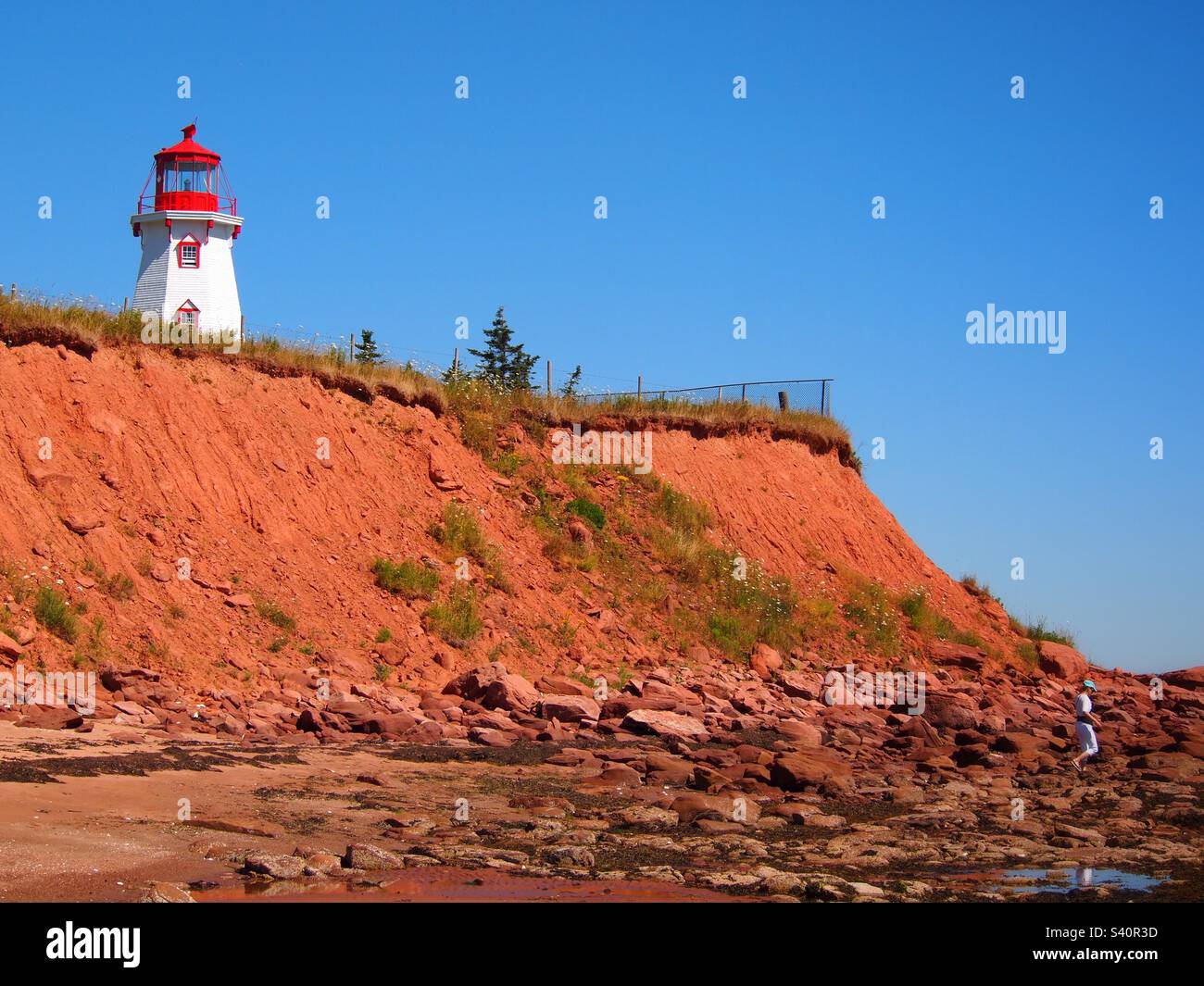 Faro rosso bianco sulla roccia rossa vicino alla costa del mare Foto Stock