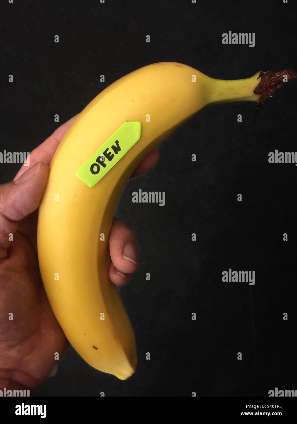 Mano che tiene una banana con un adesivo puntato e il testo aperto Foto Stock