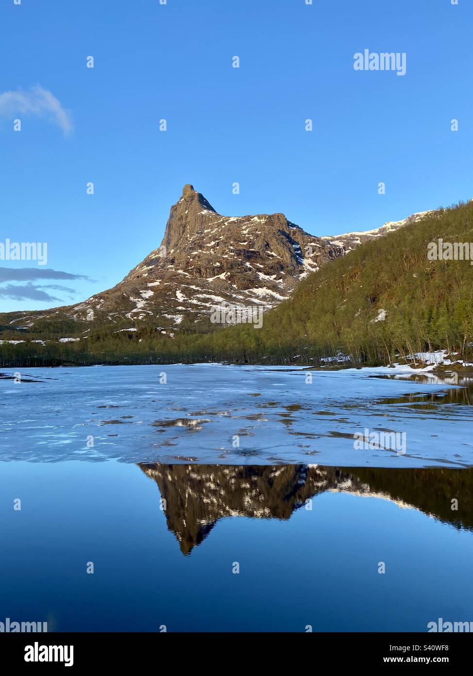 Vista della montagna Romabstøtta nella Norvegia settentrionale sopra il serbatoio d'acqua con ancora del ghiaccio su di esso. Effetto specchio nell'acqua dalla cima della montagna. Foto scattata durante le escursioni intorno a mezzanotte. Foto Stock
