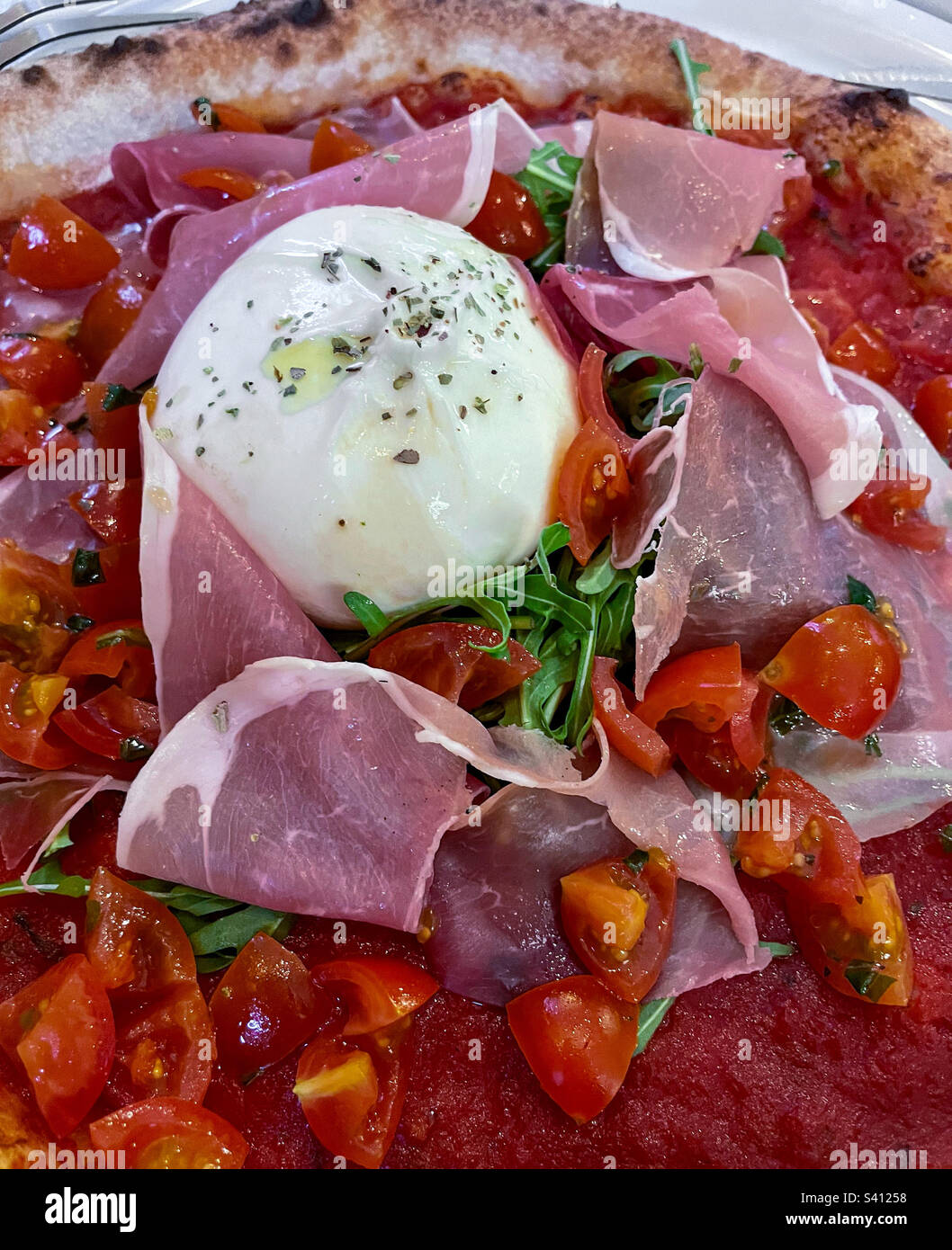 Primo piano della pizza italiana con mozzarella di bufala, pomodori a pezzetti, prosciutto, rucola, cosparsa di origano e olio d'oliva su una crosta sottile con salsa di pomodoro spessa, fotografata dall'alto Foto Stock