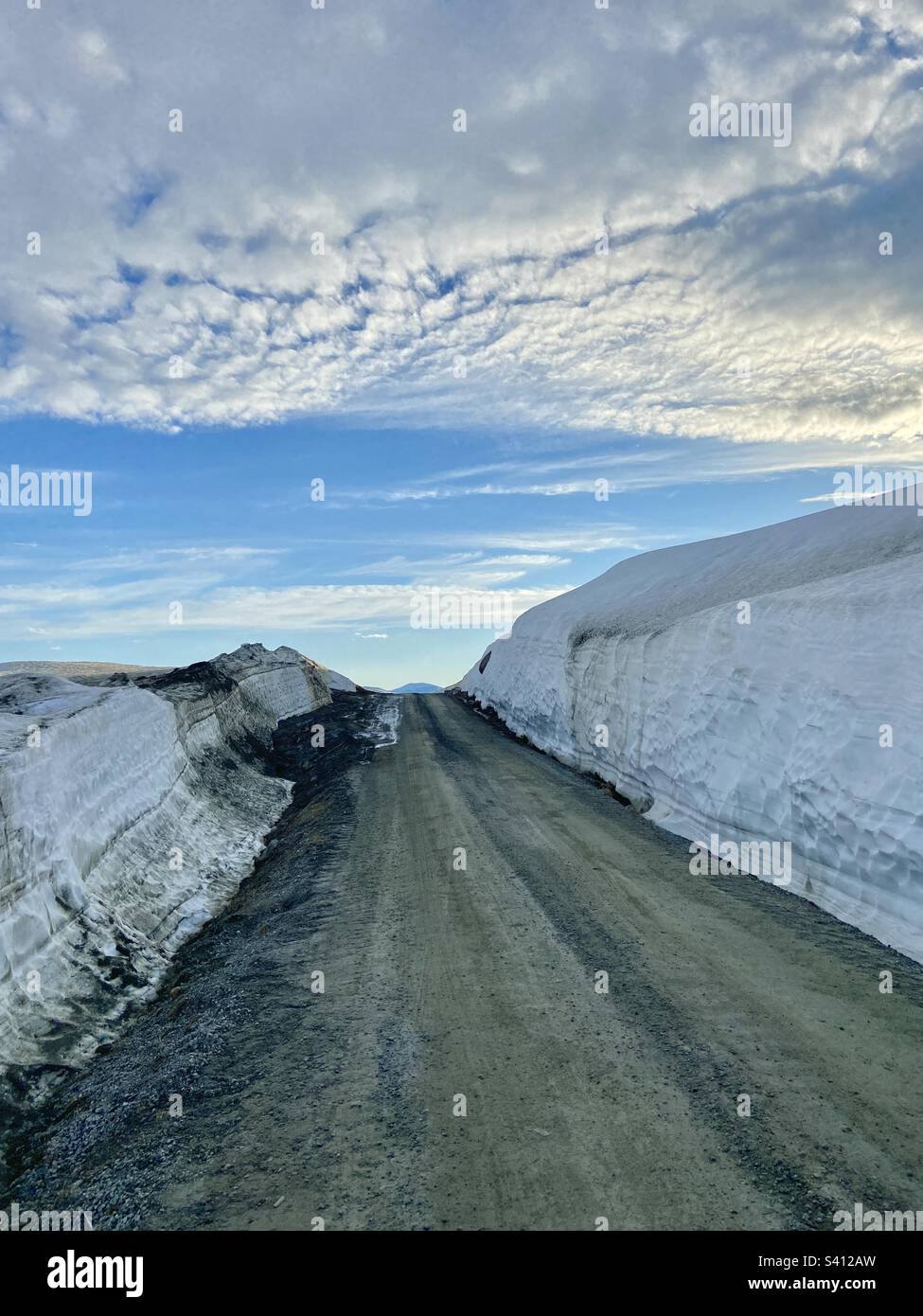 Guida su una strada di ghiaia nella Norvegia settentrionale, vicino a Fjelbu, vicino al confine con la Svezia. Nel mese di giugno, tarda sera, un sacco di neve profonda sui lati della strada. - Immagine stock catturata con smartphone