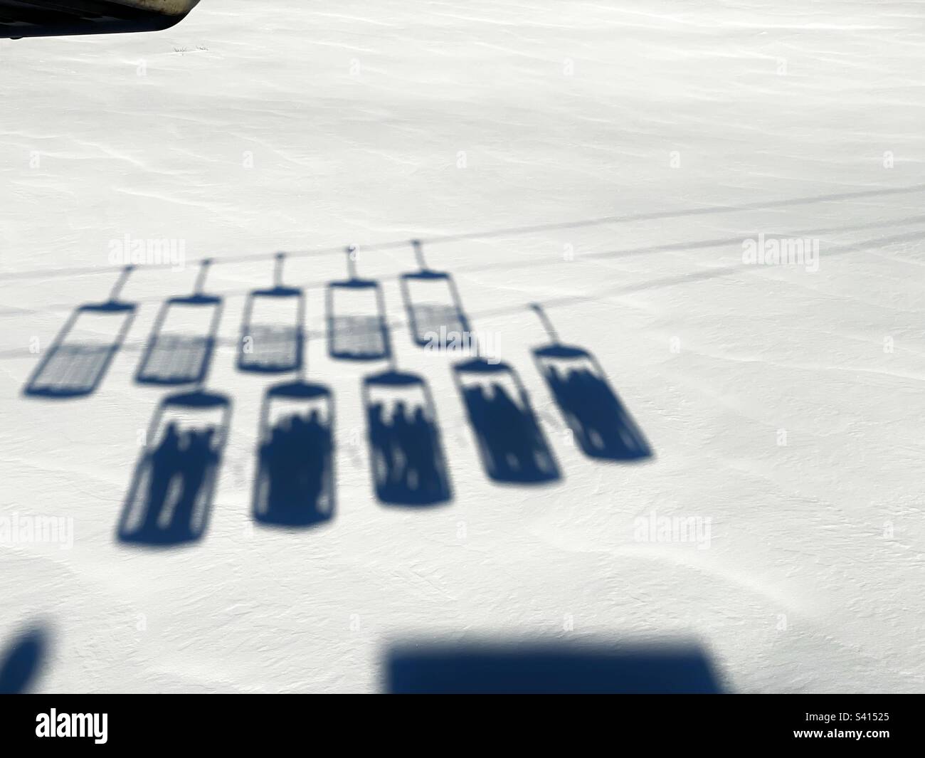 Ombre di seggiovie a secchio sulla neve fresca che portano le persone fino alle piste da sci, Alpe d’Huez. Foto Stock