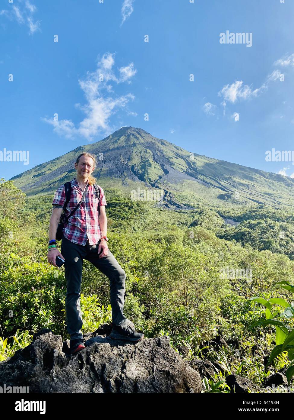 Un uomo si trova di fronte a un grande vulcano in una giornata limpida vicino a la Fortuna in Costa Rica - Immagine stock catturata con smartphone