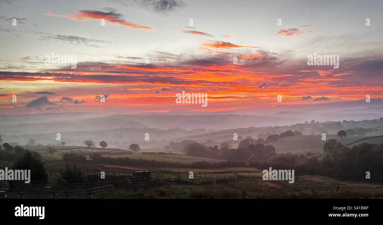 “Fuoco d’autunno” il cielo si illumina sul paesaggio dello Yorkshire, in contrasto con la bassa nebbia e la nebbia sottostante. Vista da Flockton Moor, Huddersfield, Yorkshire. Foto Stock