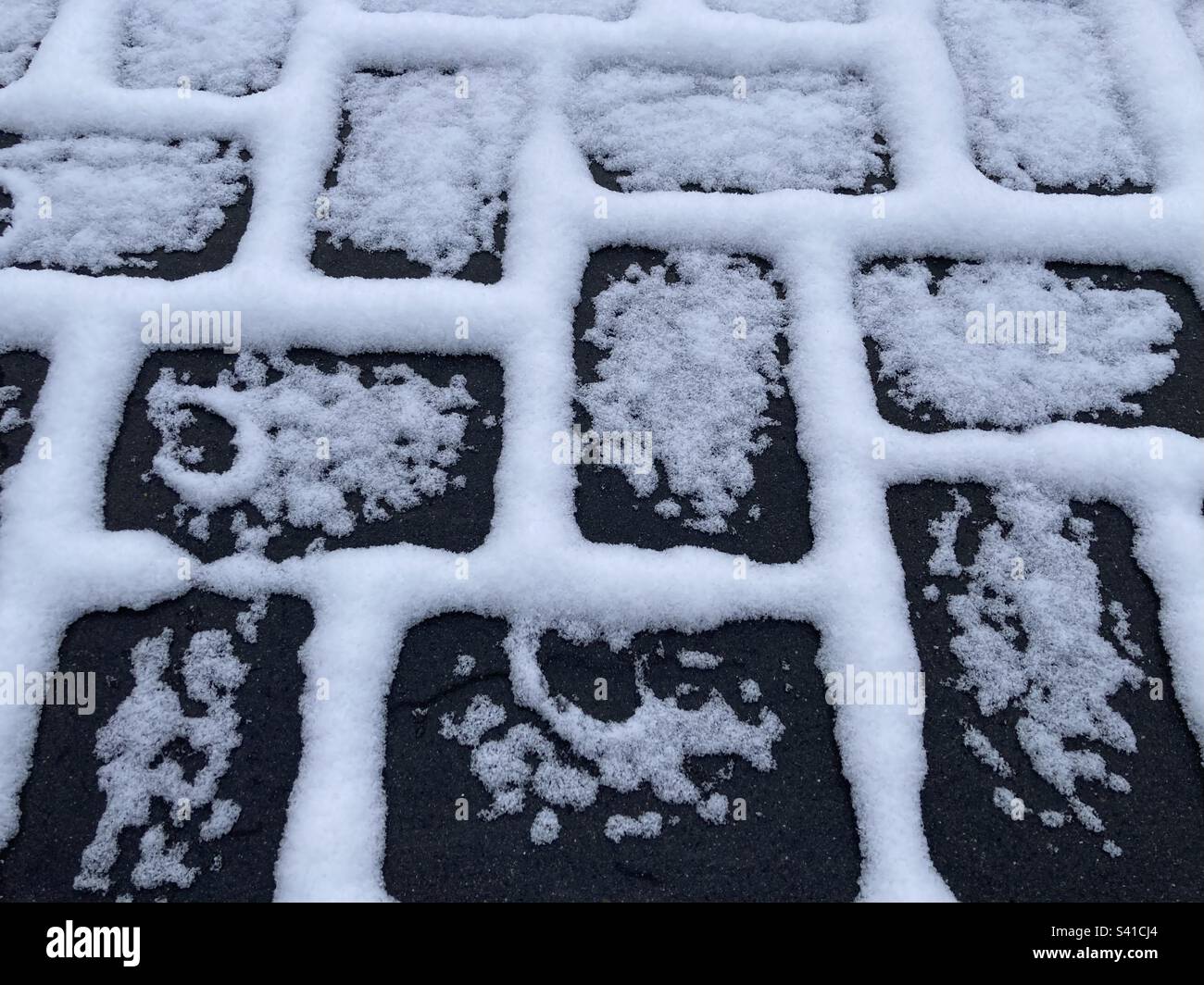 le pietre scure di un marciapiede sono bordate di neve bianca - Immagine stock catturata con smartphone