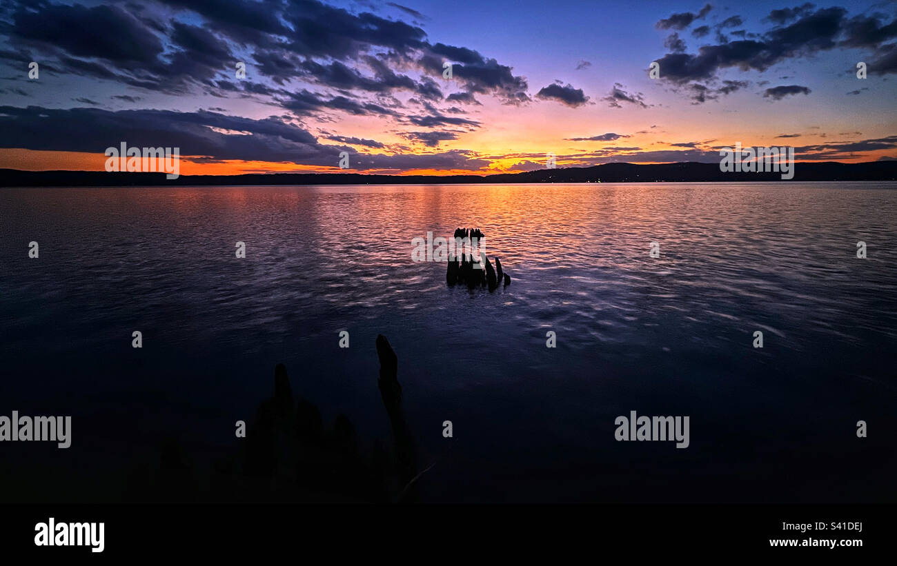 Si affaccia sul fiume Hudson al tramonto a Tarrytown, nella contea di Westchester, New York. 2022. Dall'acqua emergono vecchi supporti in legno decaduti da un lungo molo passato. Foto Stock