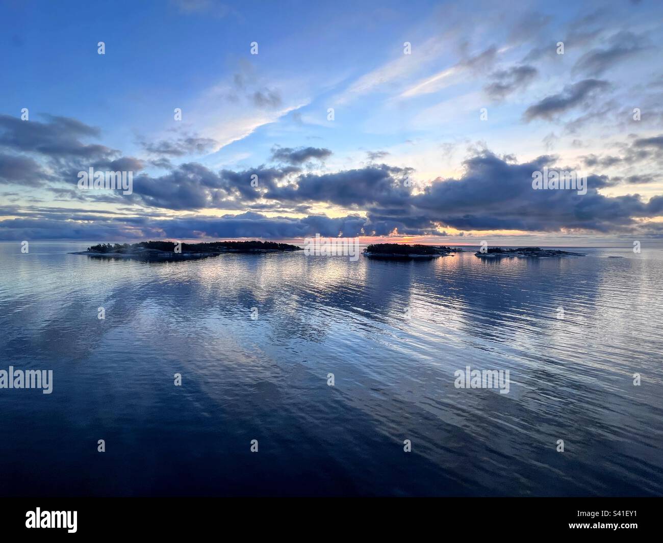 Orizzonte di scena tranquillo sopra l'alba del mare dietro le nubi scure basse con l'isola piccola e il riflesso nell'acqua - Immagine stock catturata con smartphone